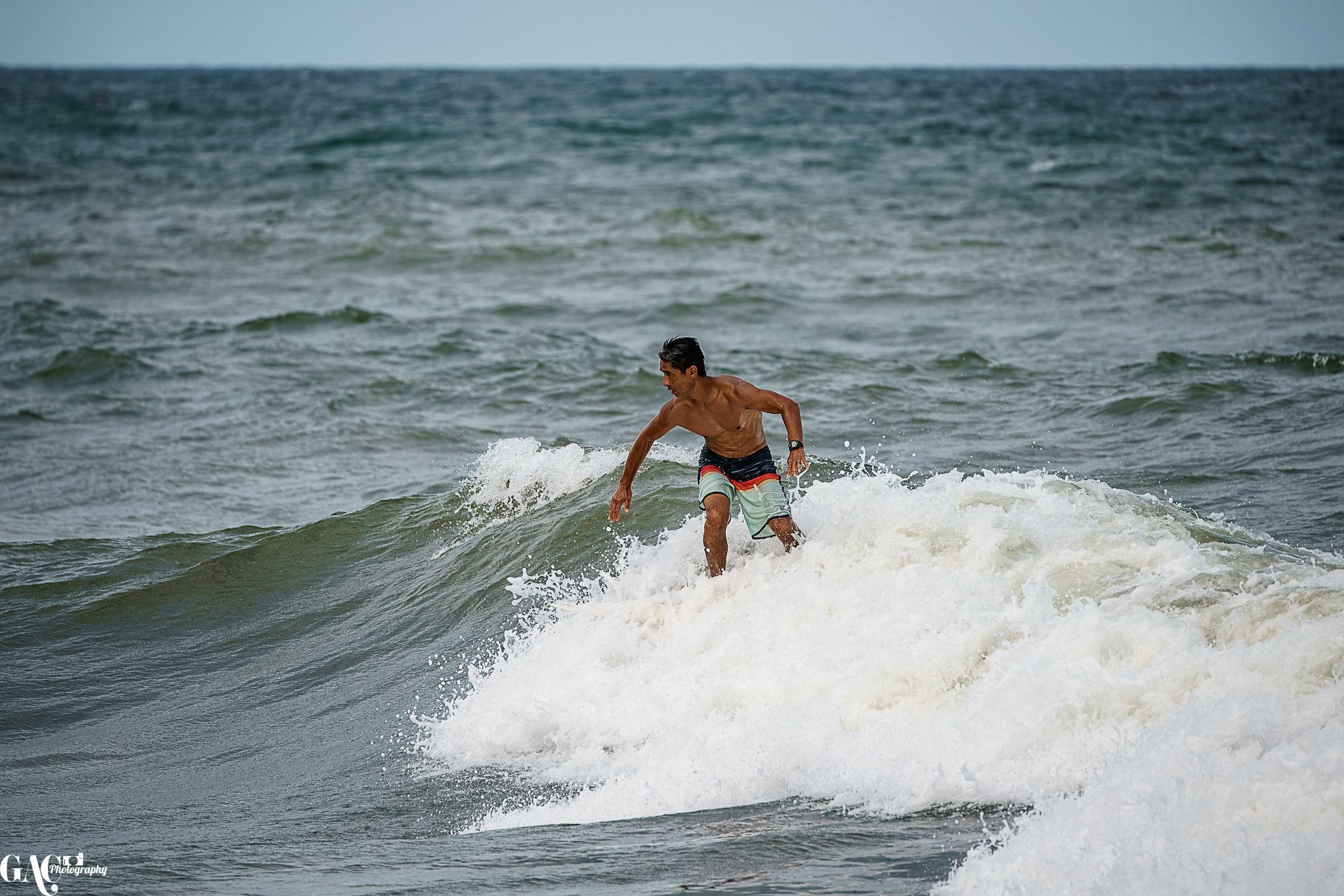 A man surfing on a small wave in the ocean, wearing swim trunks.