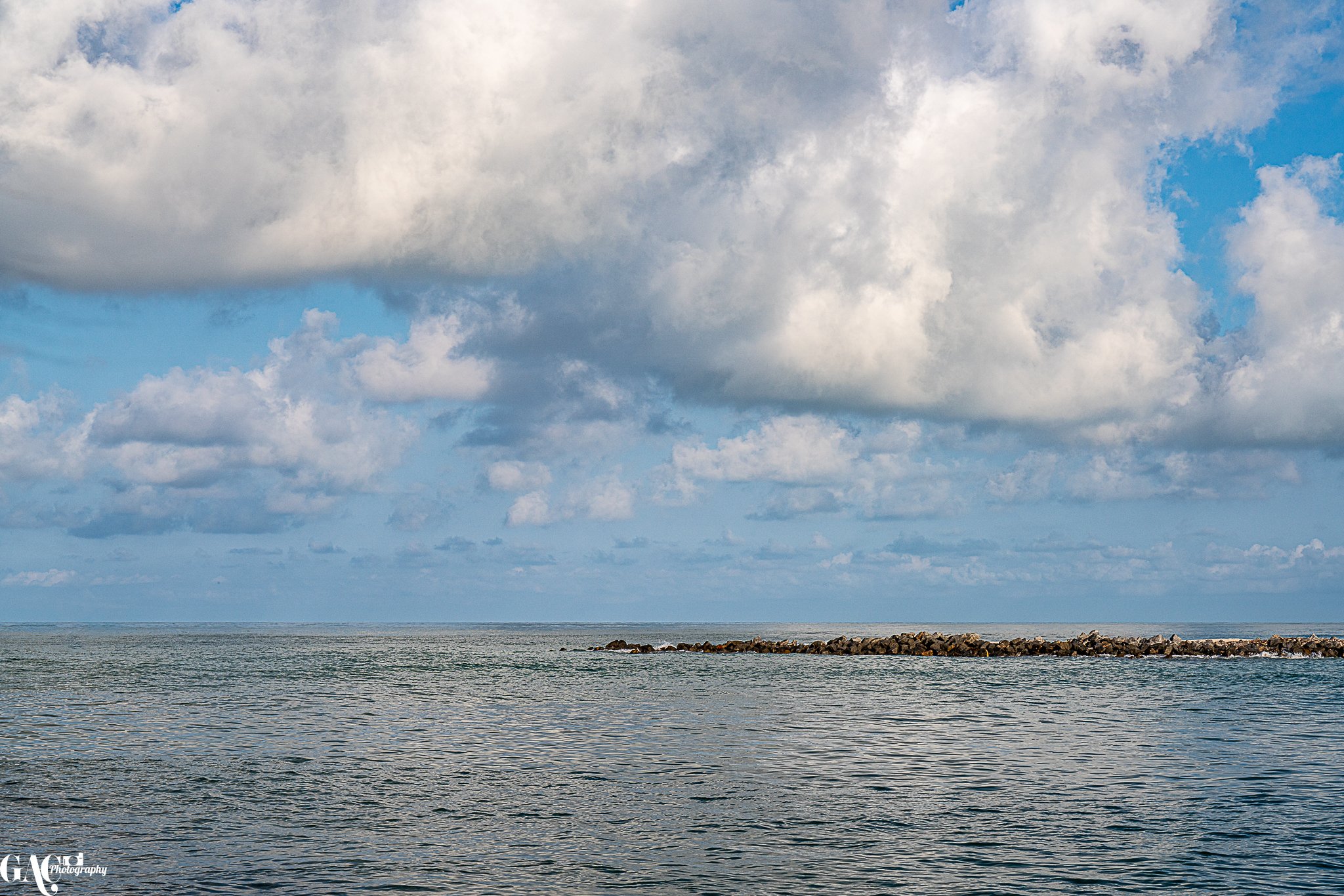 Ocean with a rocky jetty under a partly cloudy sky.