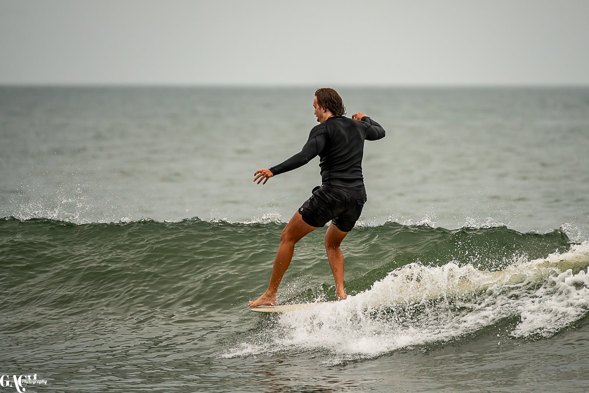A man surfing on a small wave in the ocean, wearing a black wetsuit and black shorts.