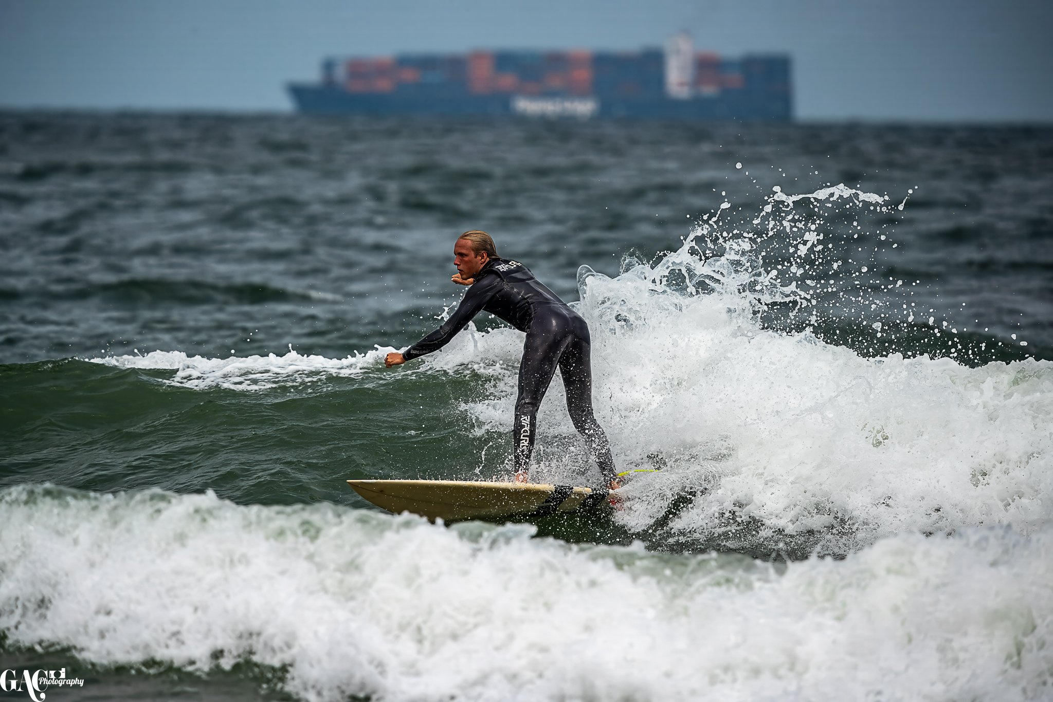 A man surfing on a wave in the ocean with a cargo ship in the background.