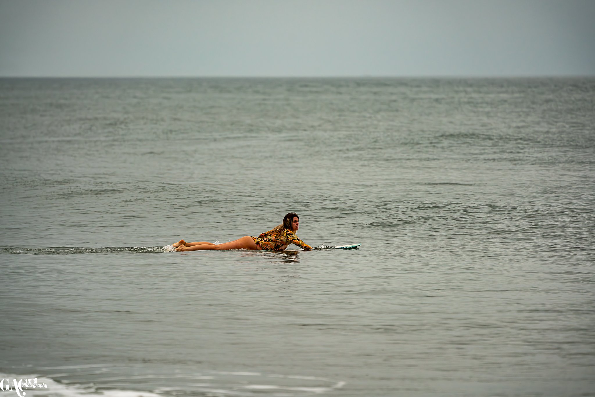 Woman in swimsuit paddling on a surfboard in calm ocean waters.