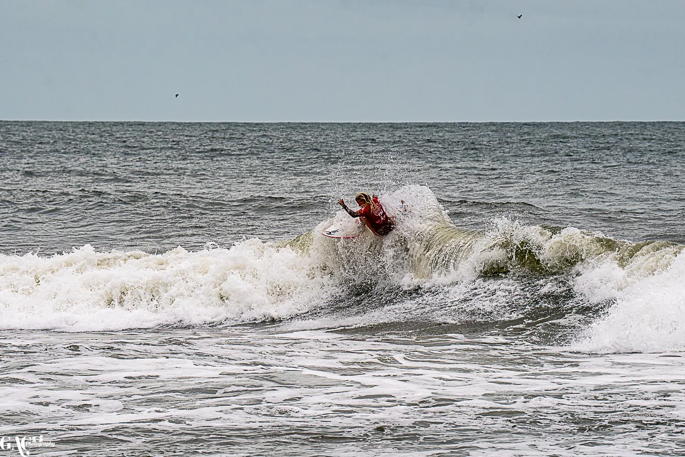 Surfer riding a wave in the ocean, with a cloudy sky overhead.