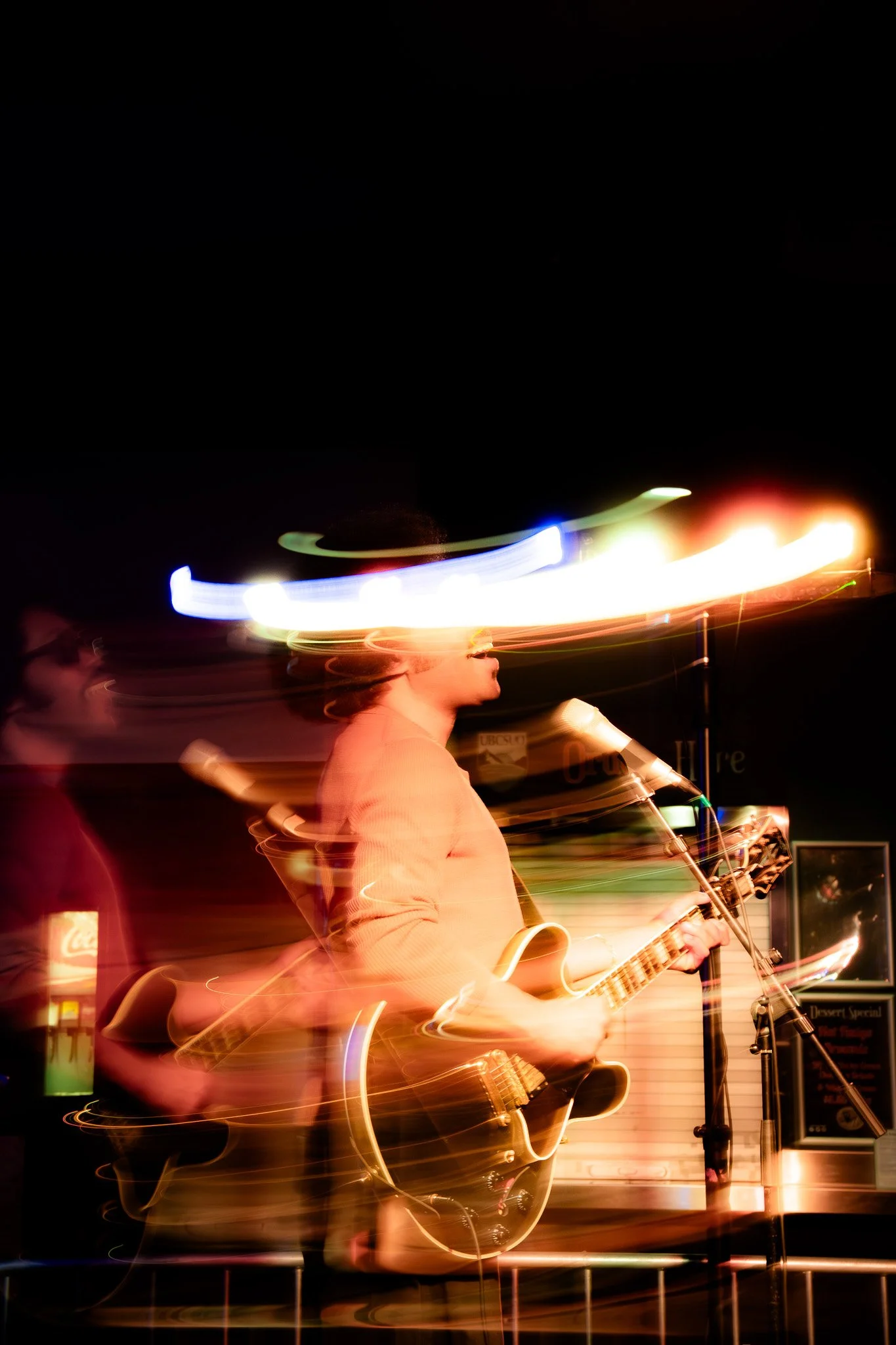 People performing music with guitars and microphones at night, with colorful light streaks across the scene, creating a motion blur effect.
