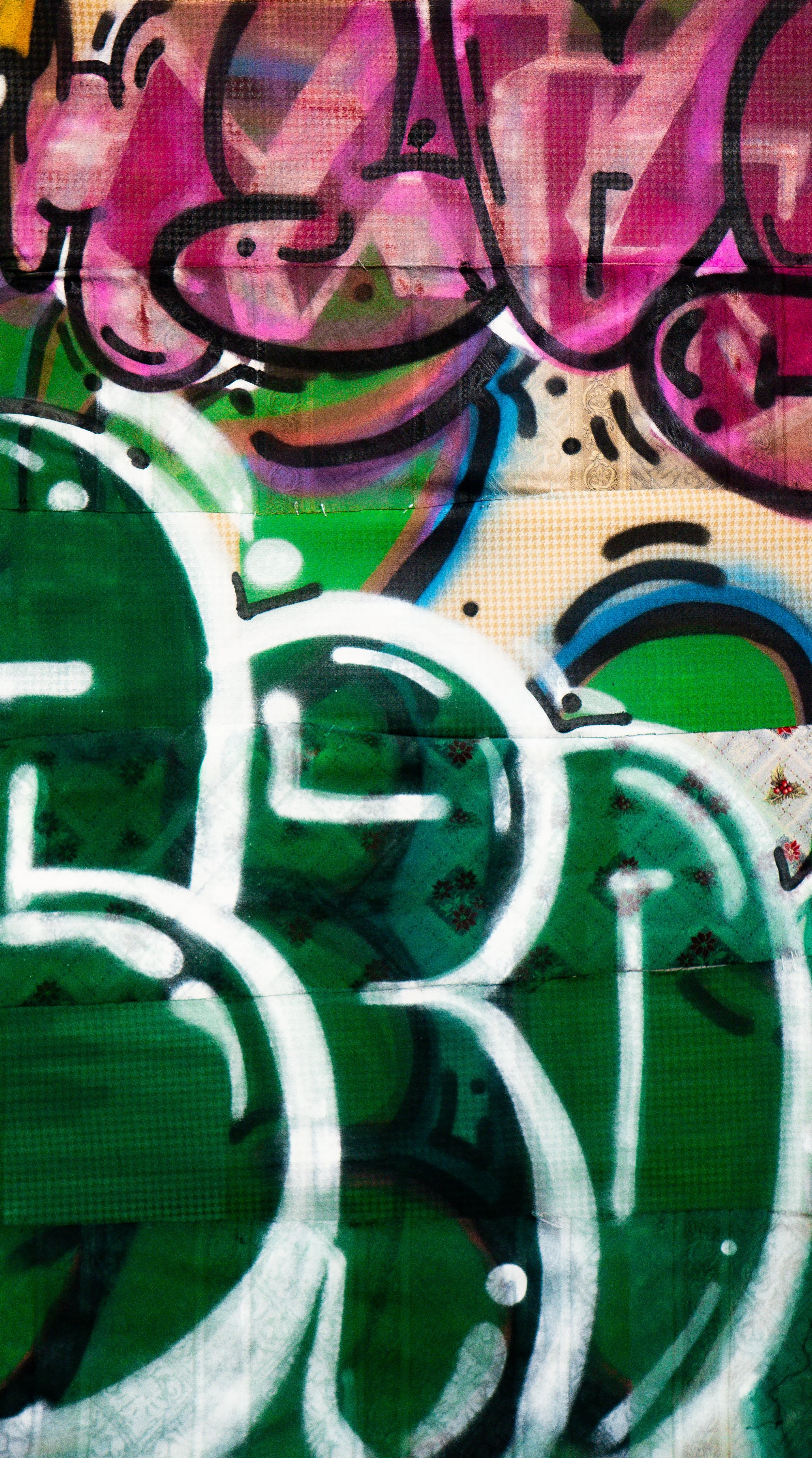 Colorful graffiti art with overlapping shapes, outlined in black, featuring bright green, pink, white, and blue sections.