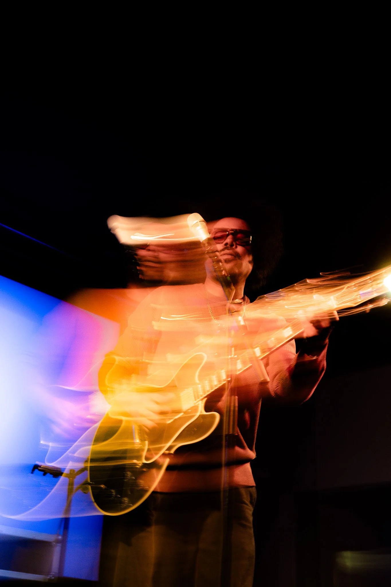 Person playing electric guitar in a dark setting with streaks of colorful lights around