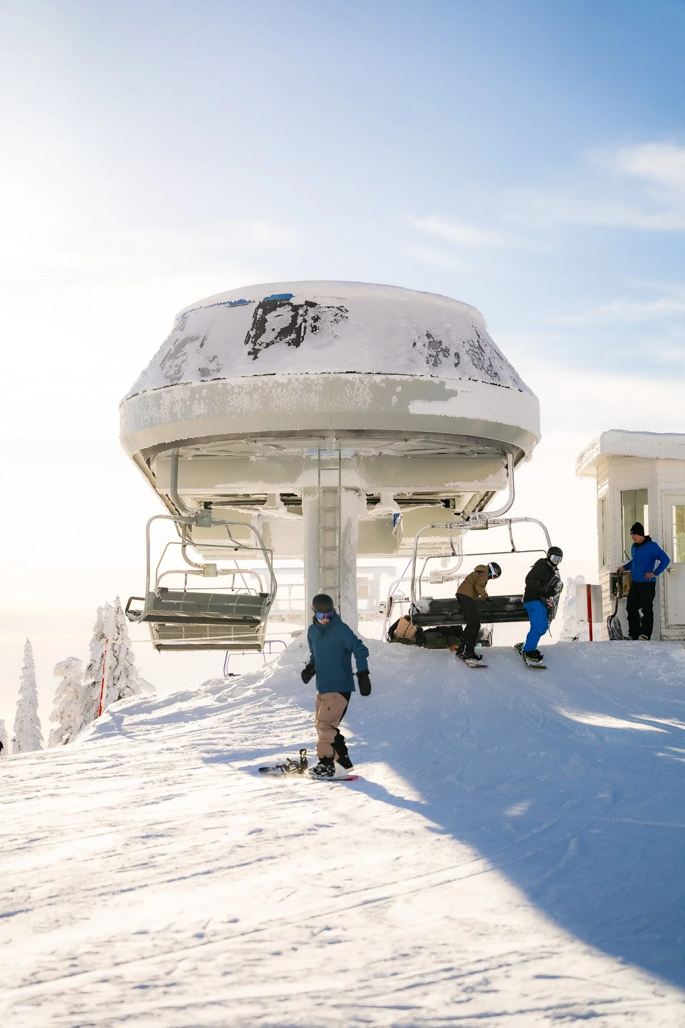 Snow-covered ski resort with skiers and snowboarders near a ski lift under a clear blue sky.