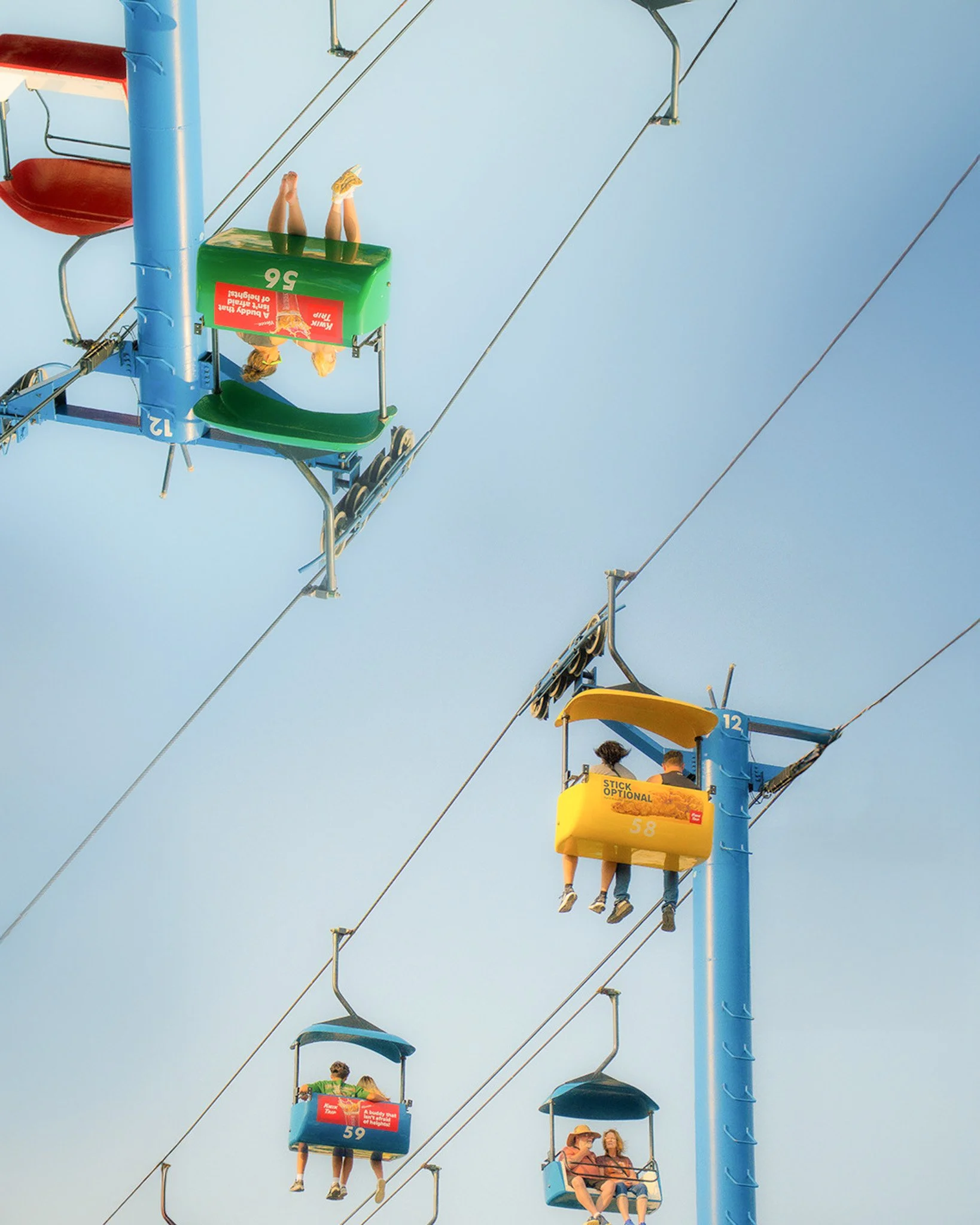 A group of people riding on colorful Ferris wheel cabins against a blue sky, with some cabins labeled and containing pairs of people.