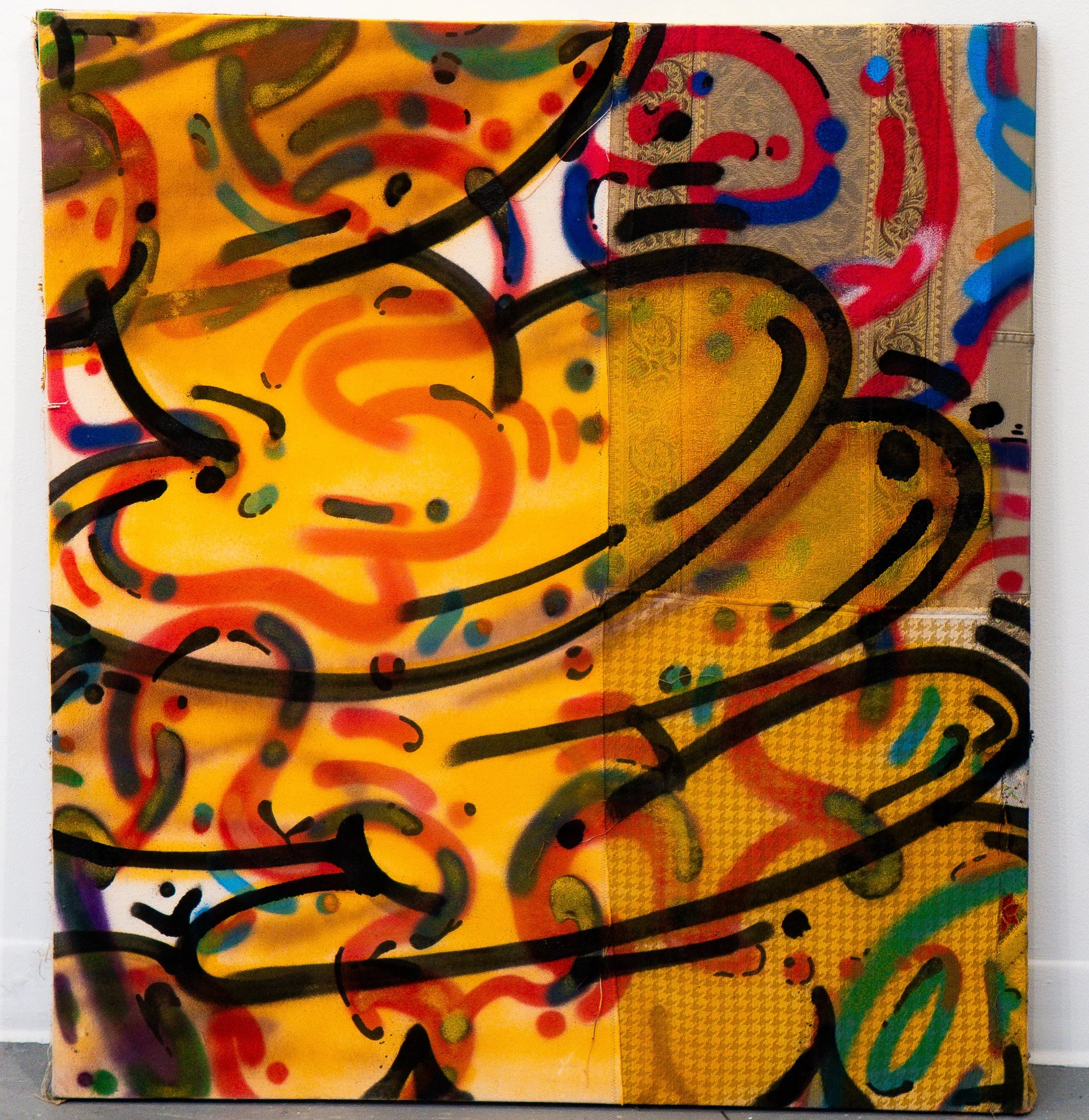 Colorful abstract painting with swirling patterns, splashes of bright colors, and bold black strokes on a canvas attached to a white wall.