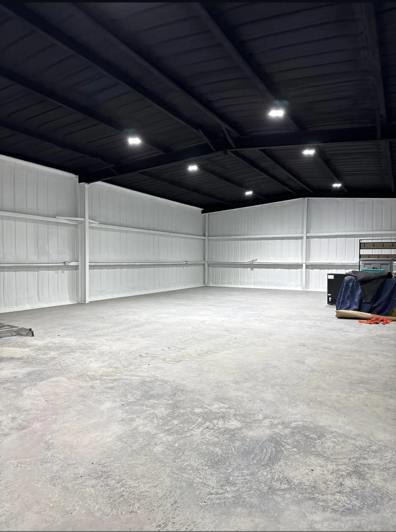 Spray foam insulated metal building interior with steel framing and concrete slab.