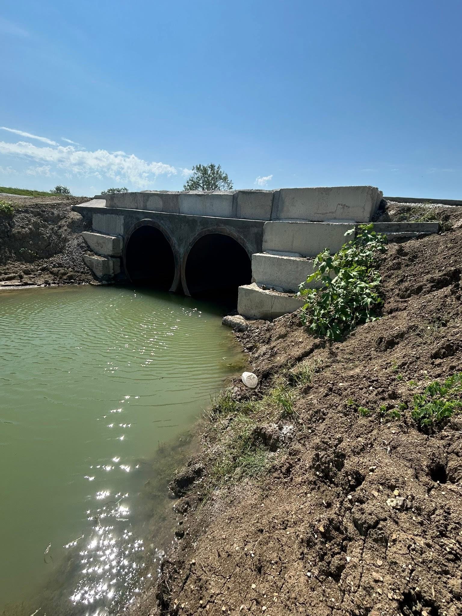 Concrete culvert bridge installation with dual drainage pipes.