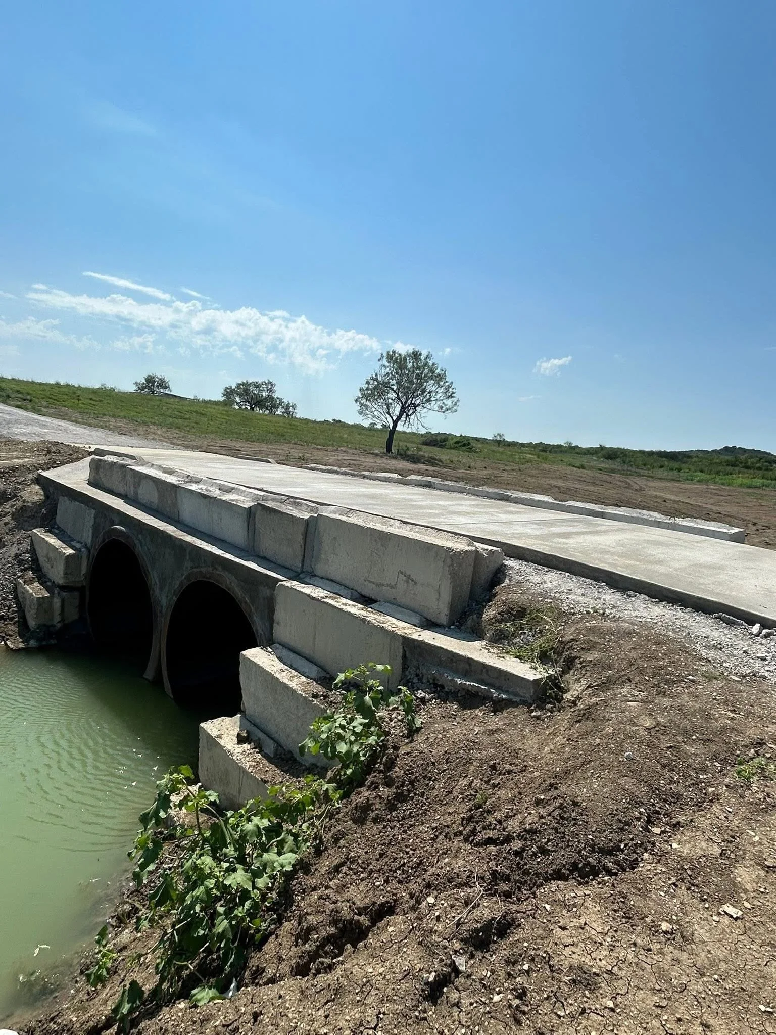 Concrete culvert bridge installation with dual drainage pipes.