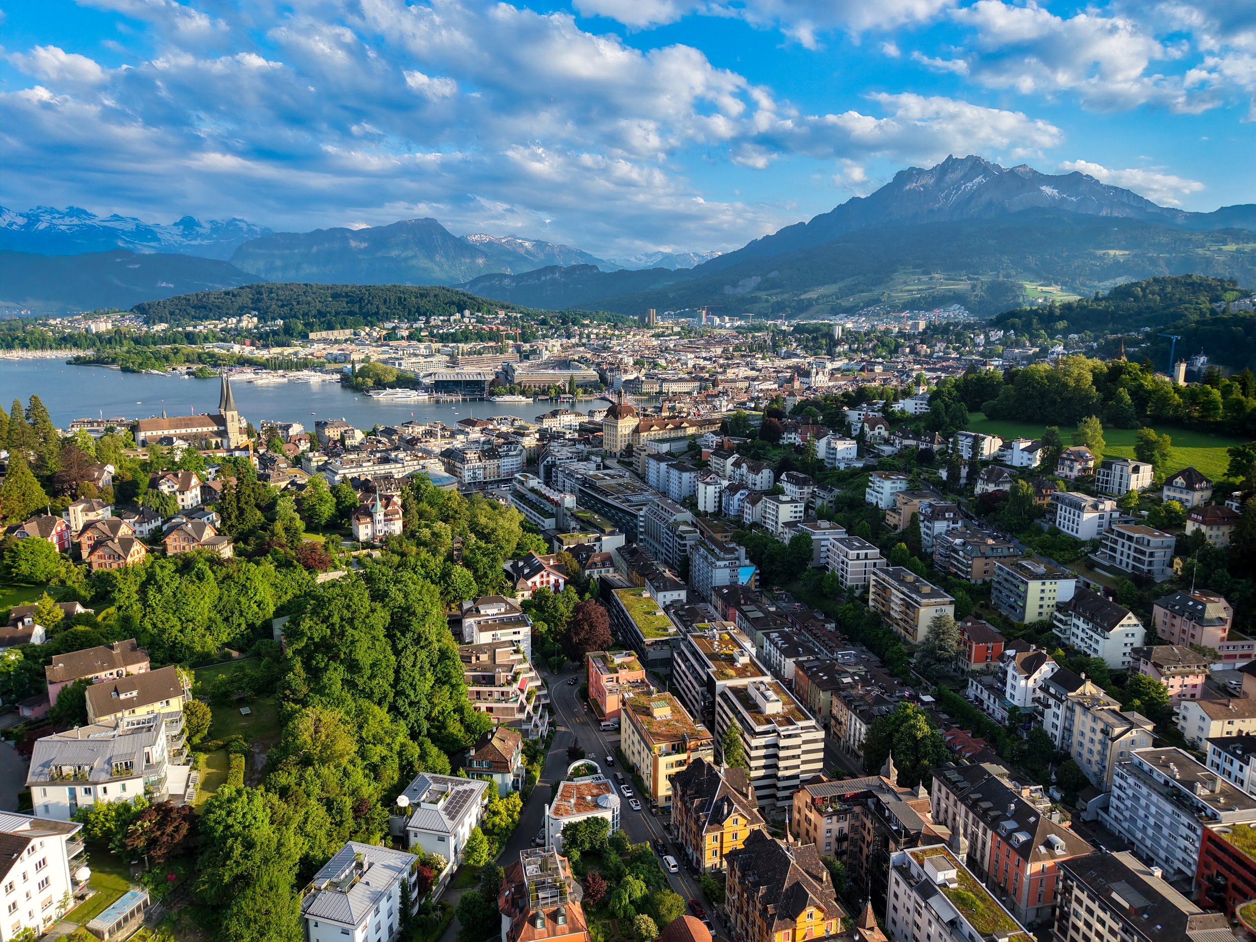 Städtische Skyline Luzern mit See, Bergen und grünen Hügeln bei sonnigem Himmel.