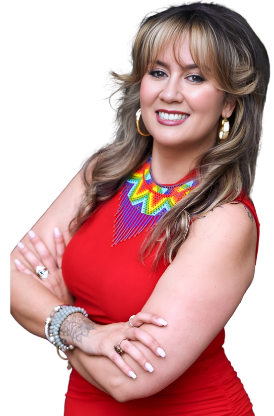 A woman with blonde hair and a bright smile wearing a red sleeveless dress and colorful beaded necklace and jewelry, posing with arms crossed.