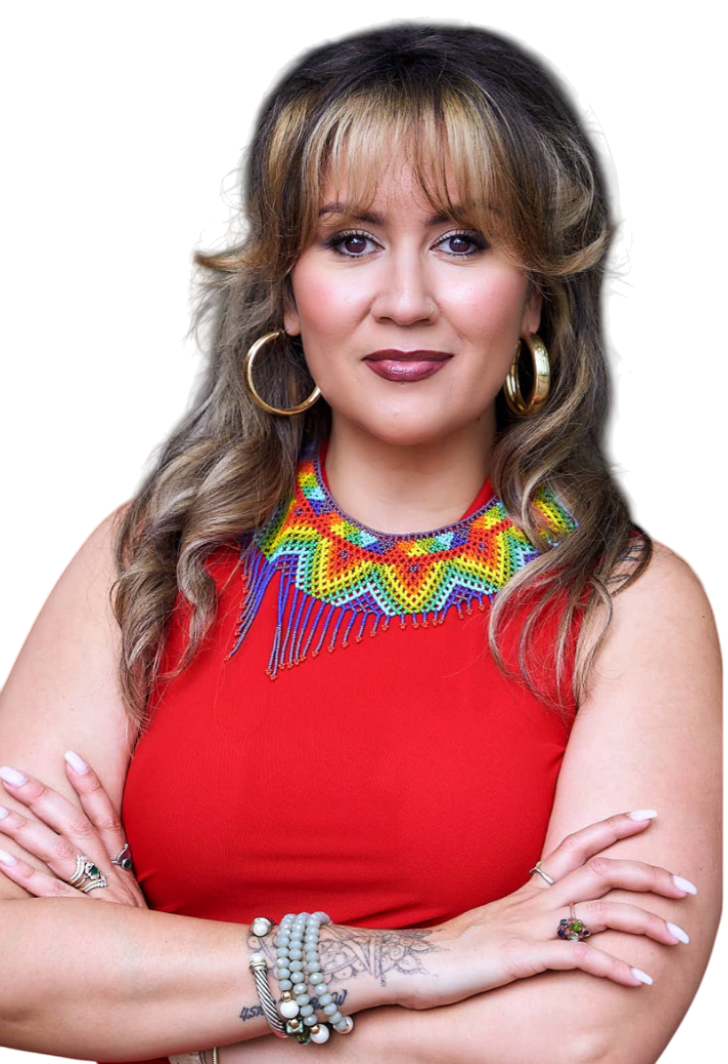 A woman with long, wavy hair wearing a red sleeveless top, large hoop earrings, and a colorful beaded necklace. She has her arms crossed, showing multiple bracelets and rings, and has a confident expression.