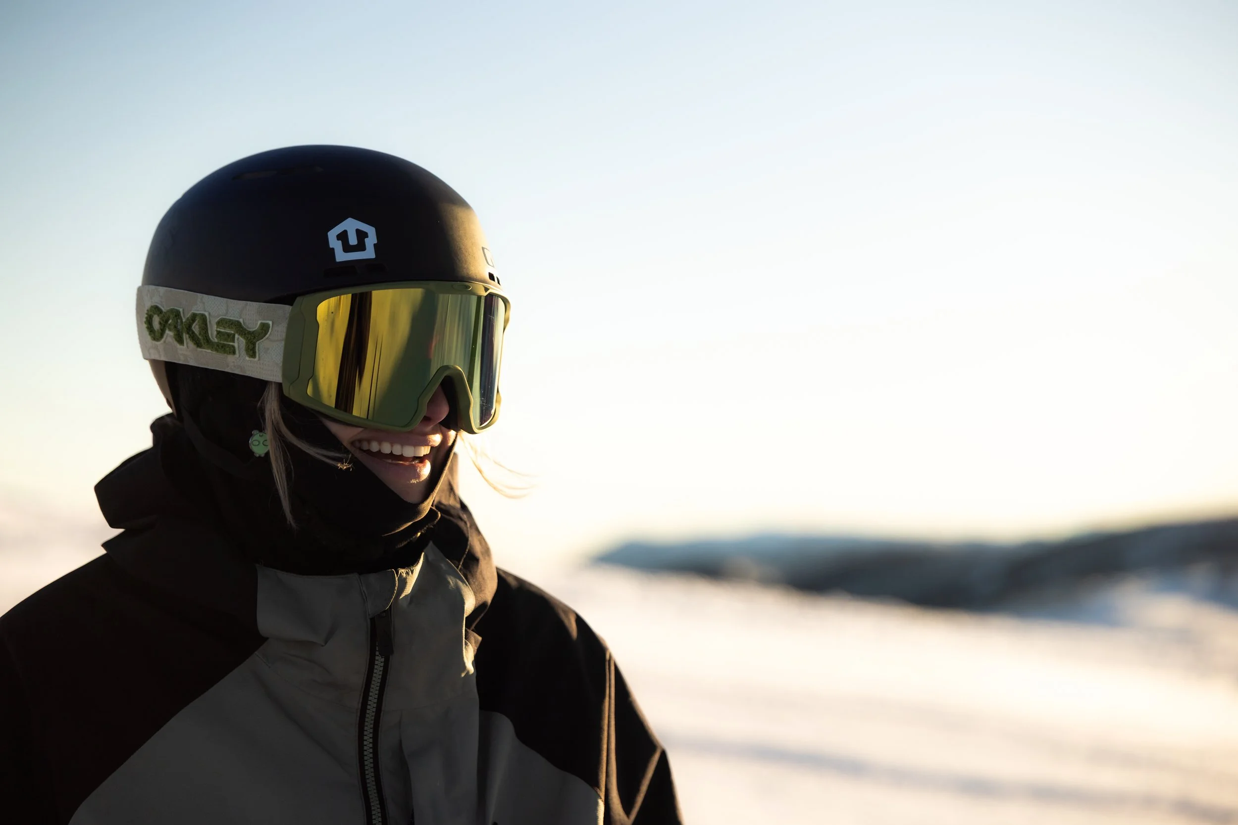 A snowboard girl smiling outdoors in a snowy landscape at sunrise.