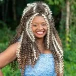 Woman with curly silver and black hair, smiling outdoors in a wooded area.
