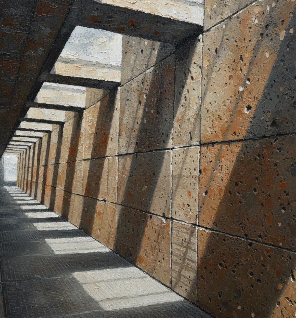 Photo of a long corridor with large stone walls and a ceiling, casting striped shadows on the tiled floor. The walls are made of rough, textured stone blocks in shades of brown and tan.