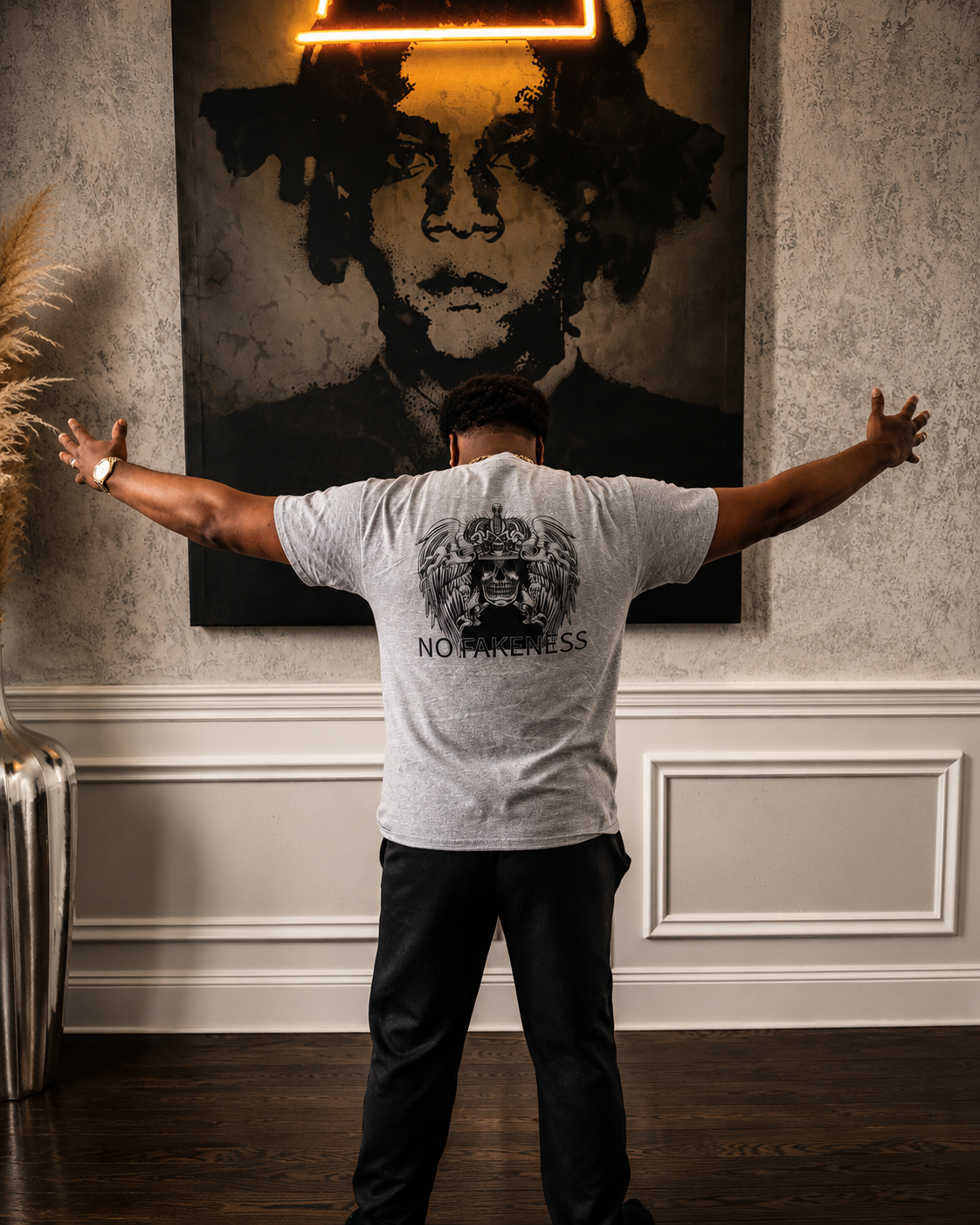 A man standing with arms outstretched in front of a large artwork of a person's face on the wall.