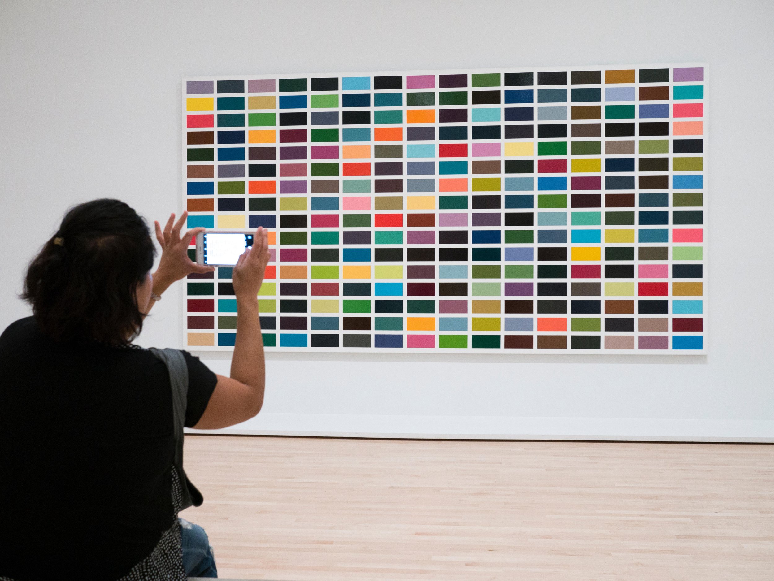 A woman in a museum gallery takes a photo of 1025 Farben (1025 Colours) by German artist Gerhard Richter.
