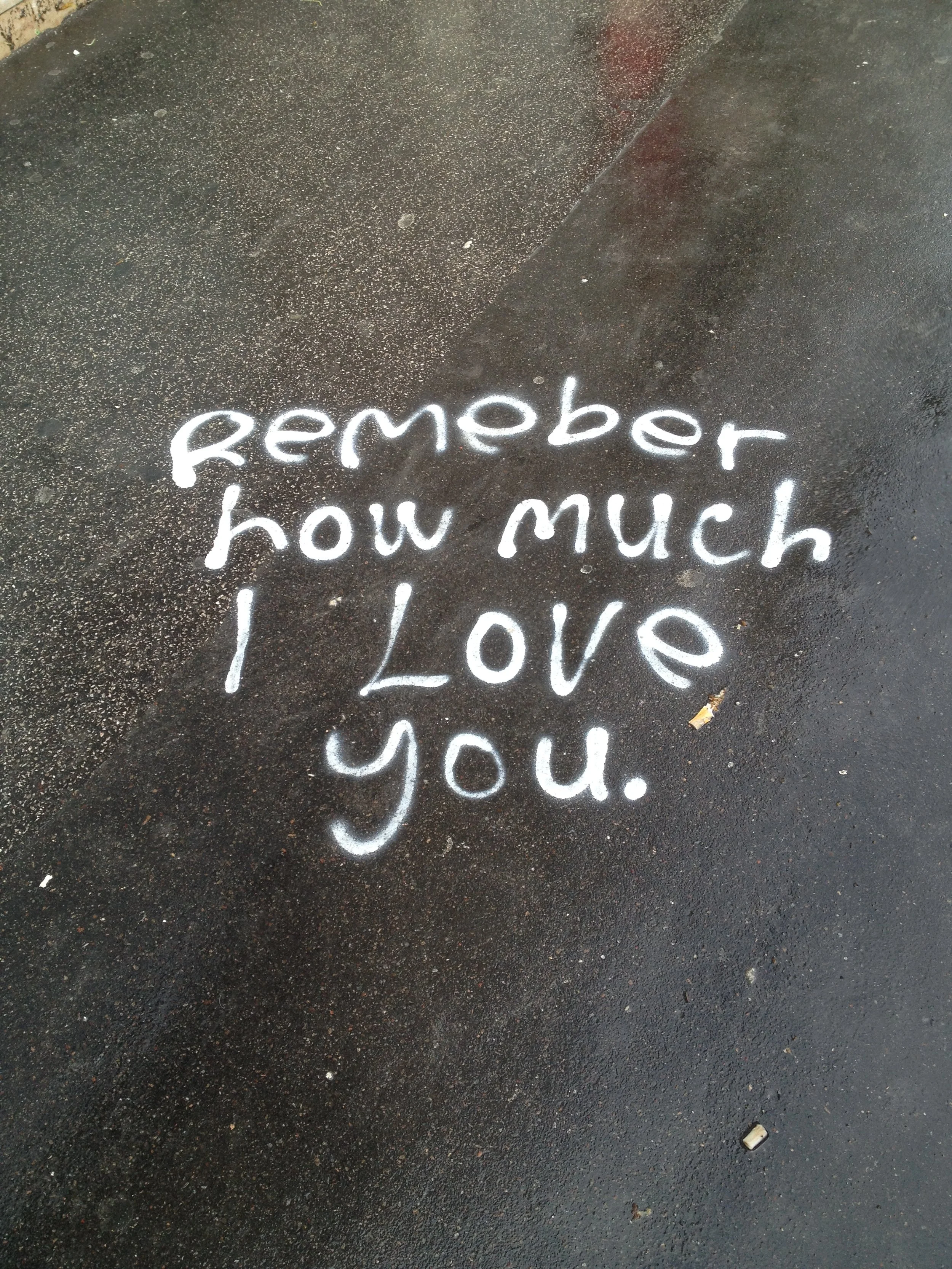 White spray-painted message on dark concrete pavement reads, 'remember how much I Love you.'