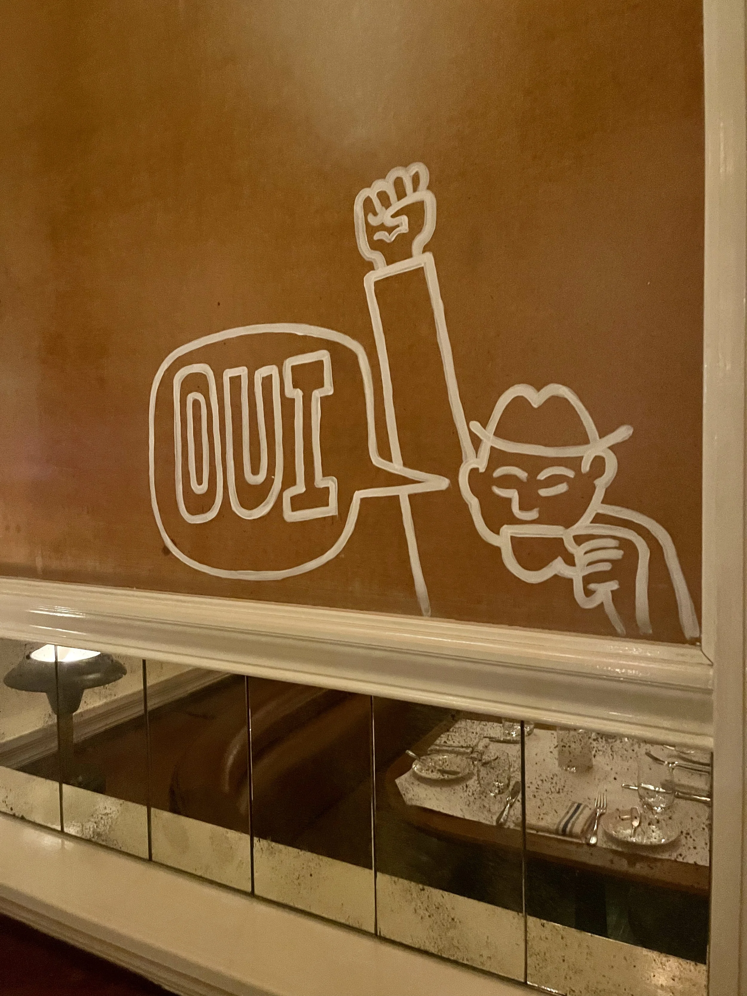 A drawing of a smiling person with glasses and a hat, holding a drink, with the word 'OUI' in a speech bubble, and a raised fist next to their head.