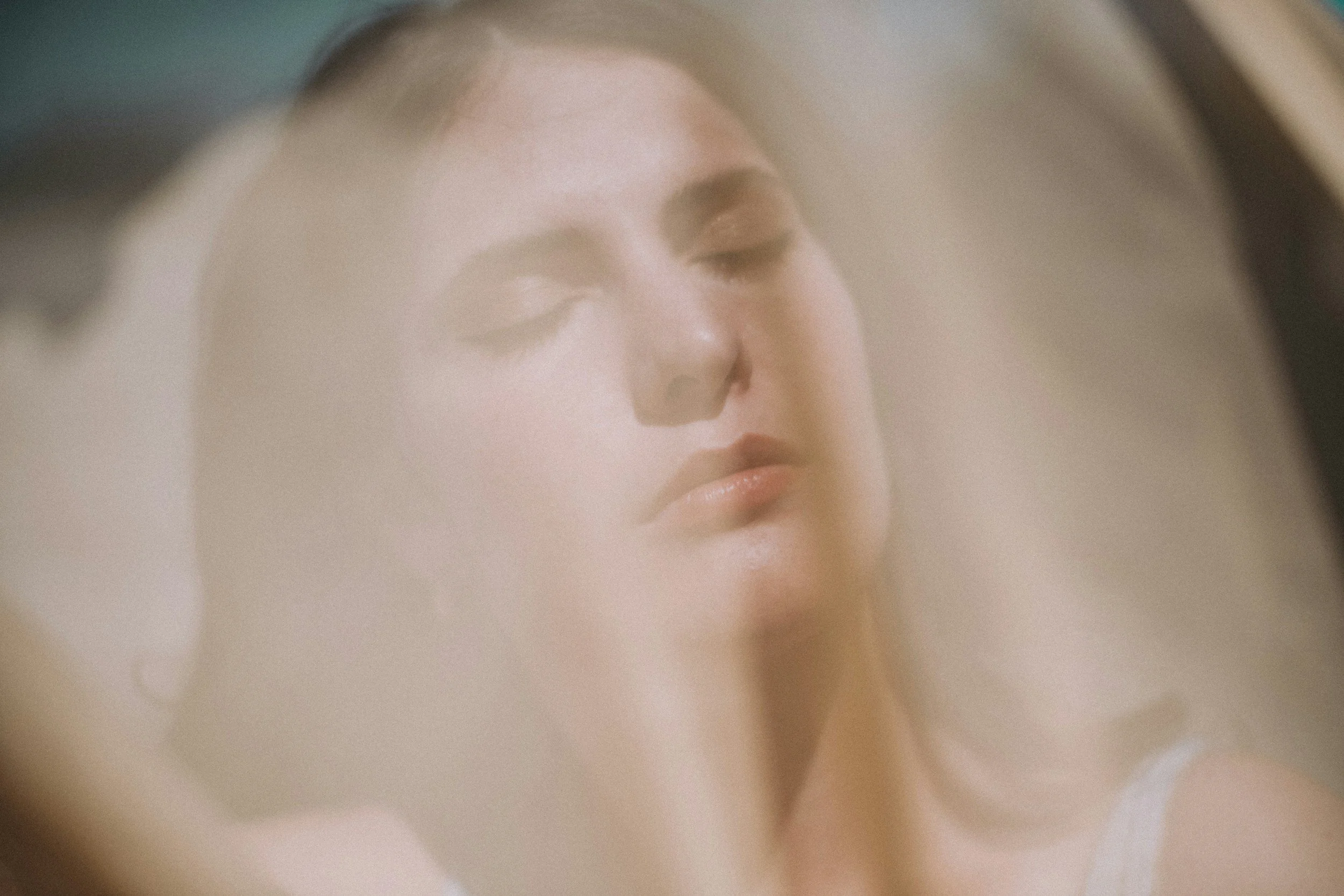 Close-up of a person's face, likely a woman with closed eyes and light makeup, seen through a crystal or glass object