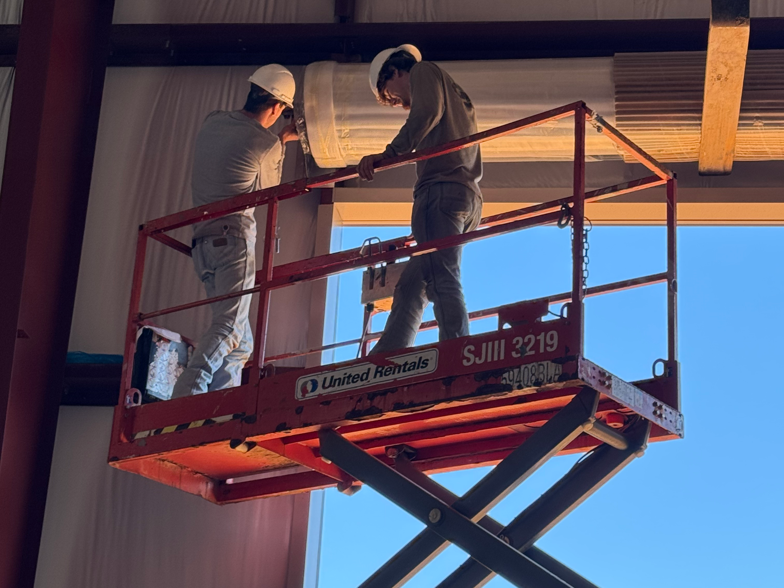 Two workers on a red lift platform working on a garage door install