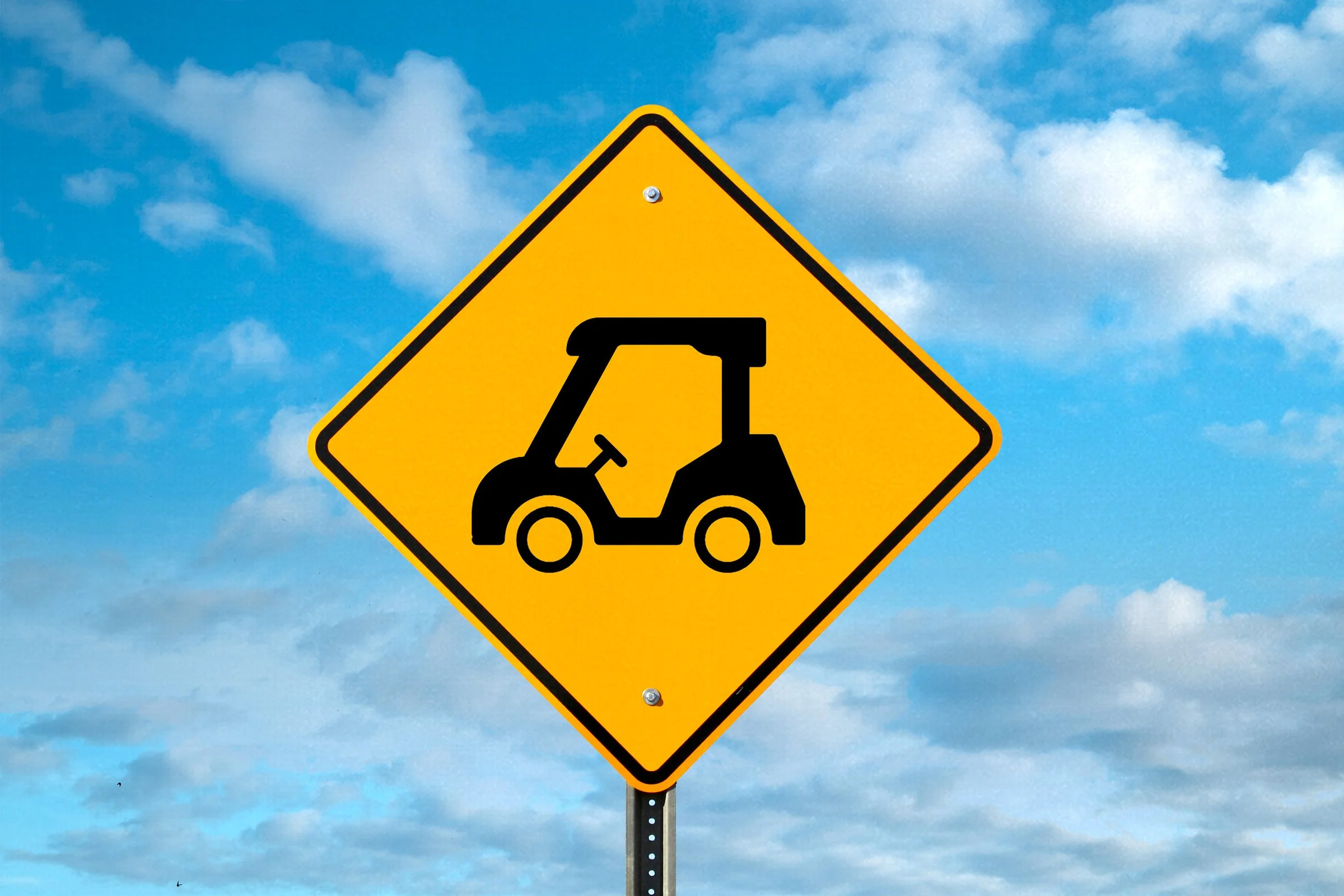 Yellow diamond-shaped road sign with a black silhouette of a tractor, under a partly cloudy sky.