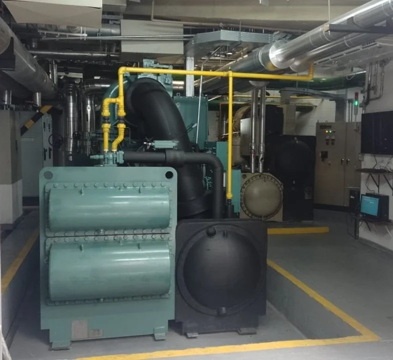 Sala de máquinas industrial com Chiller York, tubulações e painéis elétricos.
