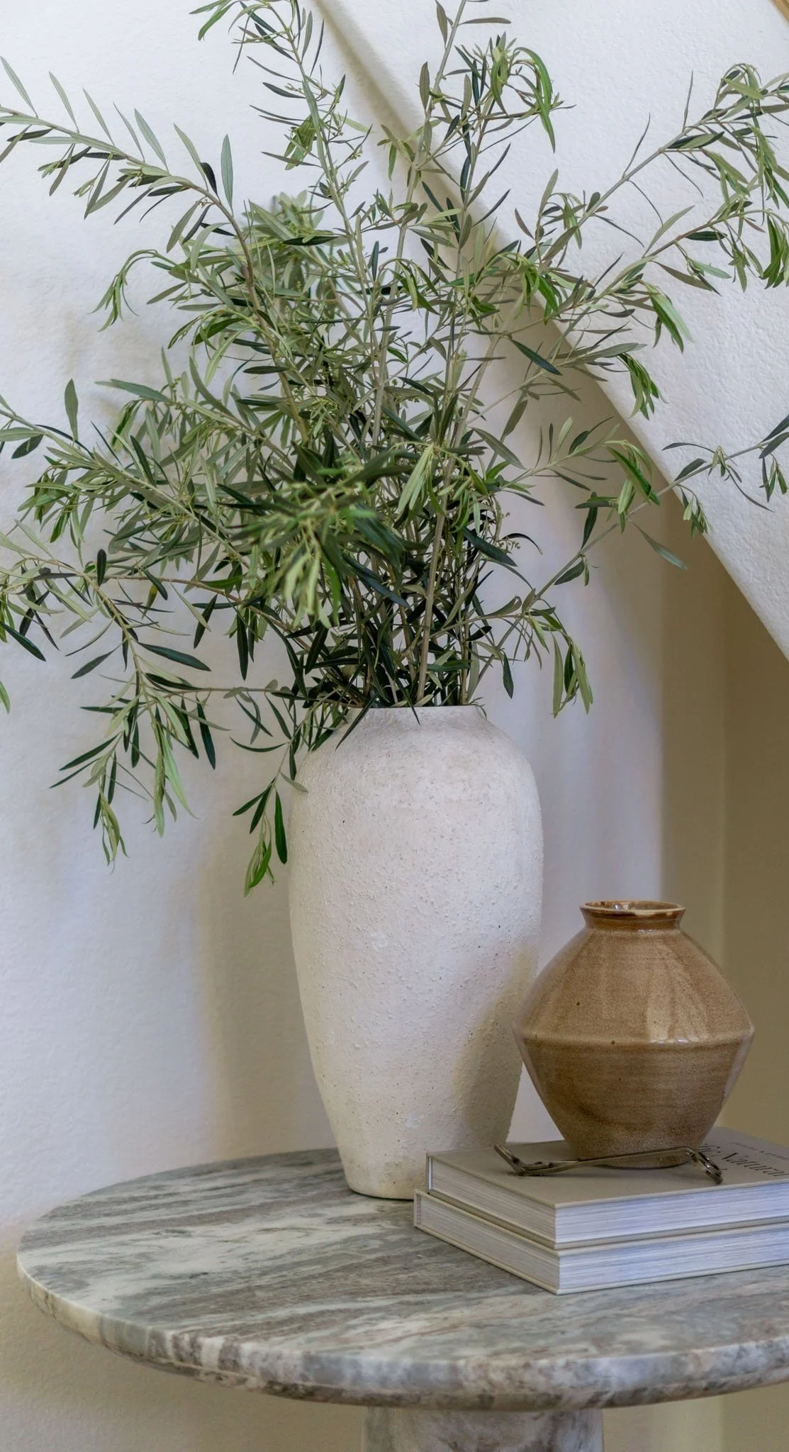 Decorative marble table with a white vase containing green branches, a brown ceramic vase, and two stacked books.