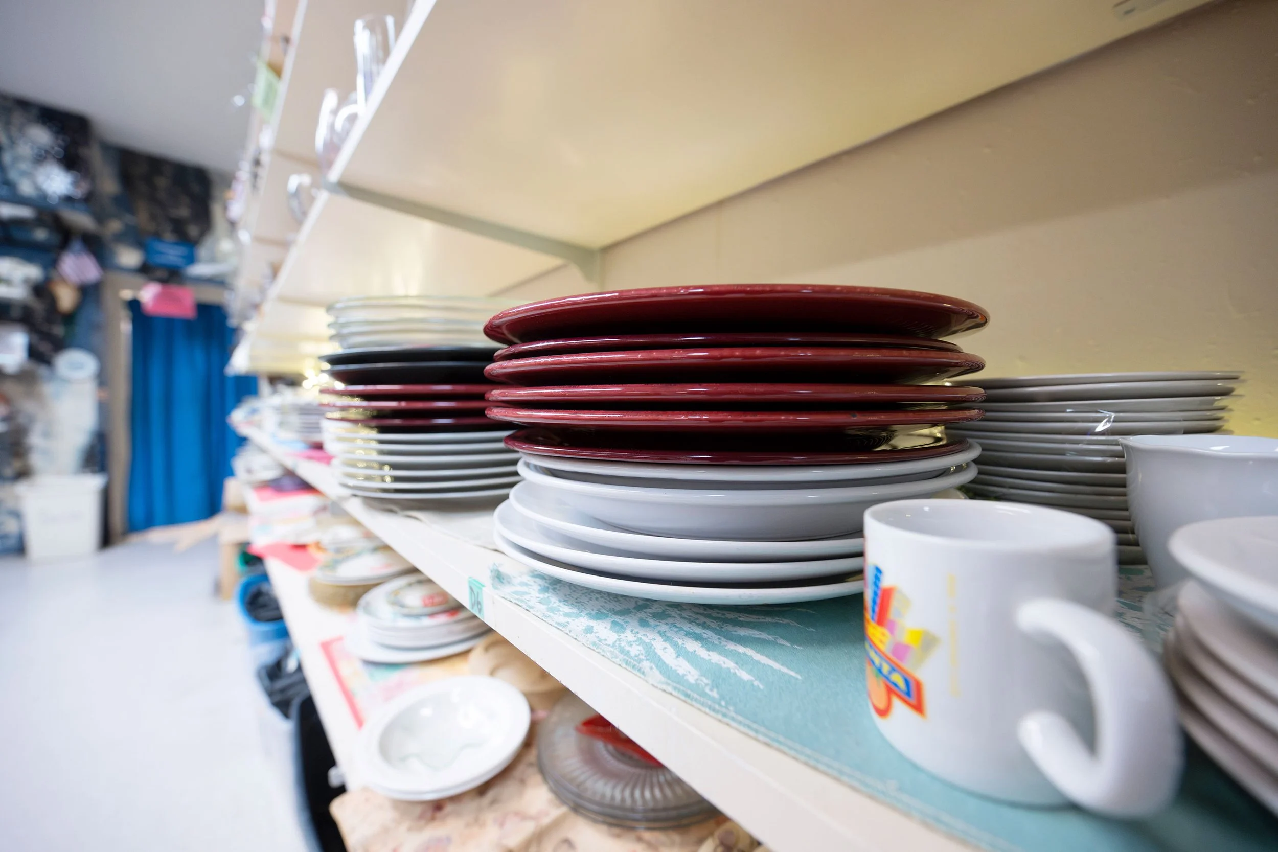 Stacks of plates and cups on a store shelf, with shelves and store items in the background.