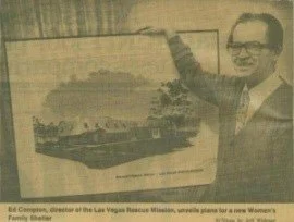 A man in glasses smiling and pointing at a framed picture of a boat on water.