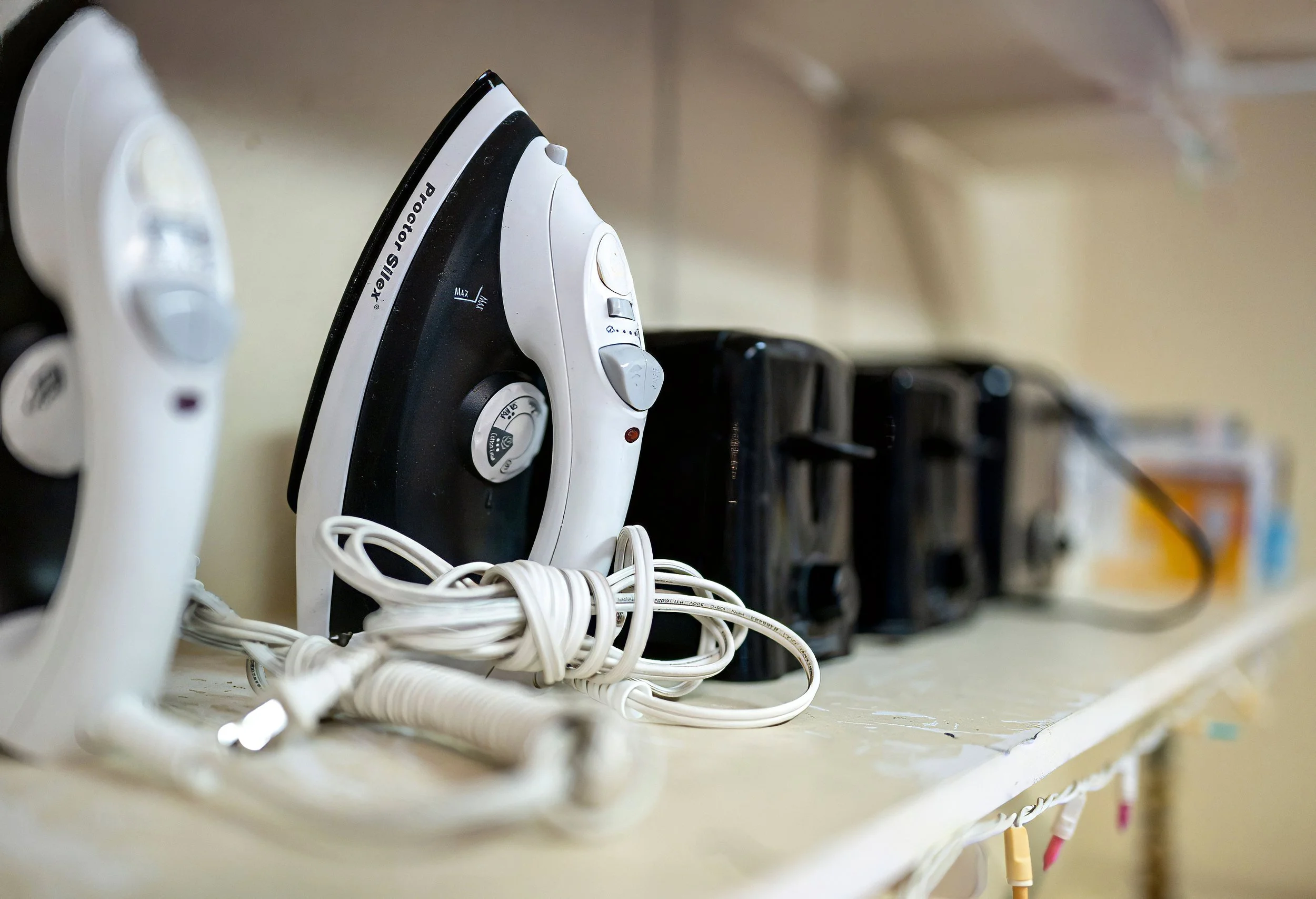 Multiple irons plugged into power strips on a cluttered shelf, with cords tangled in the foreground.