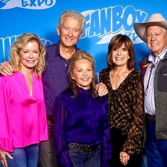 Group of five older adults, three women and two men, smiling and posing for a photo together in front of a blue background with text that says 'FANBOY EXPO'.