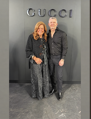 A woman and a man standing side by side in front of a Gucci store sign, smiling at the camera.