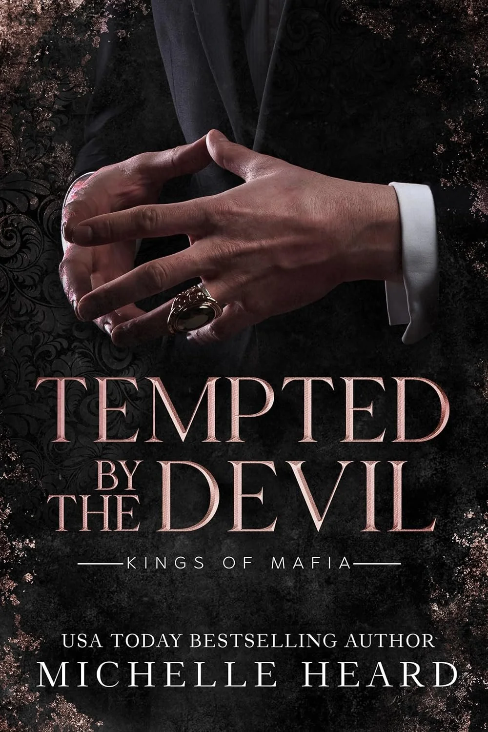 Book cover titled 'Tempted by the Devil: Kings of Mafia' by Michelle Heard, featuring a man in a black suit with a white shirt, clasping his hands with a large ring on his finger, against a dark floral background.