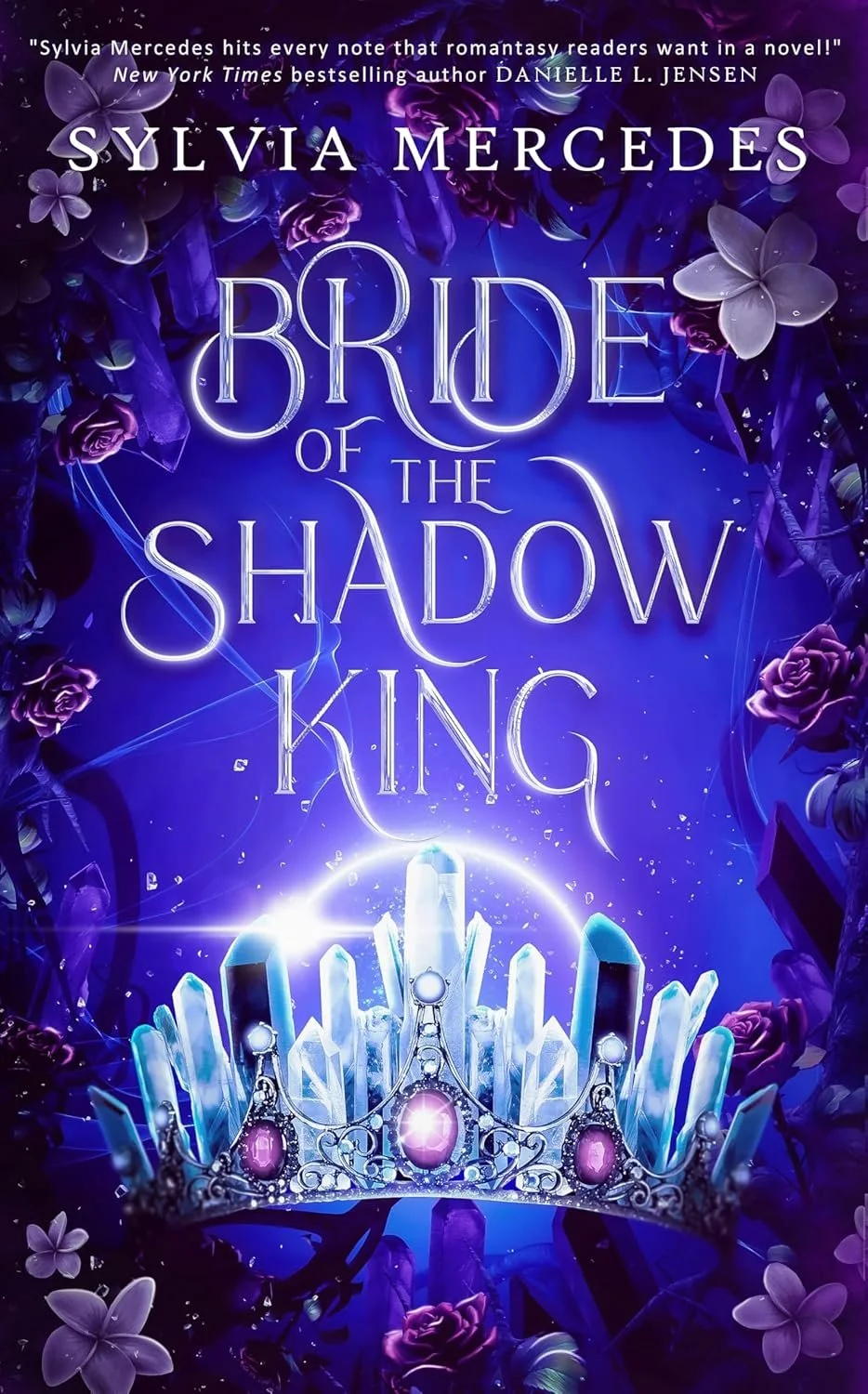 Digital fantasy book cover titled 'Bride of the Shadow King' by Sylvia Mercedes, featuring a glowing crown with purple gemstones, surrounded by purple flowers and crystals in a mystical, dark blue background.