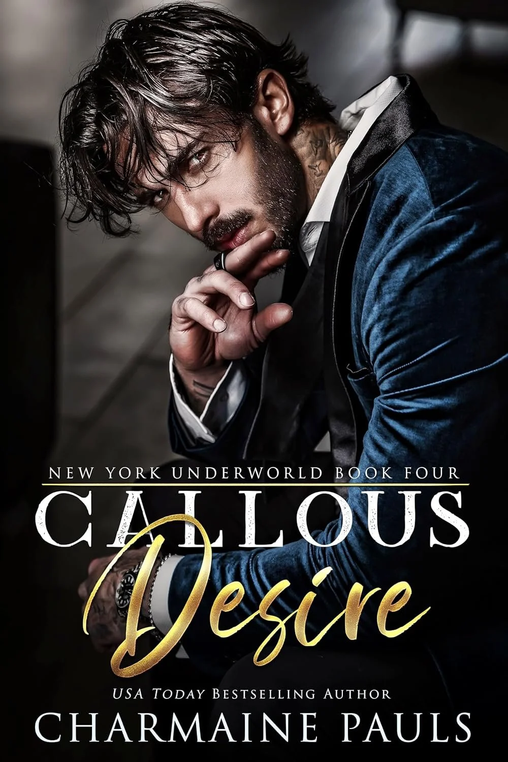 Cover of a book titled "Callous Desire" by Charmaine Pauls featuring a man with dark, wavy hair and a beard, wearing a dark blue velvet jacket and white shirt, posing with his hand near his chin.