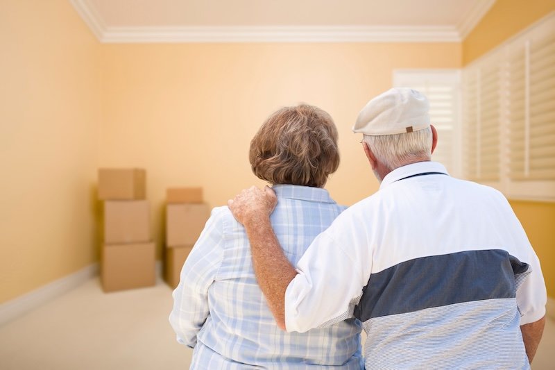 Downsizing For Seniors Or Retirement - senior couple embracing looking at moving boxes