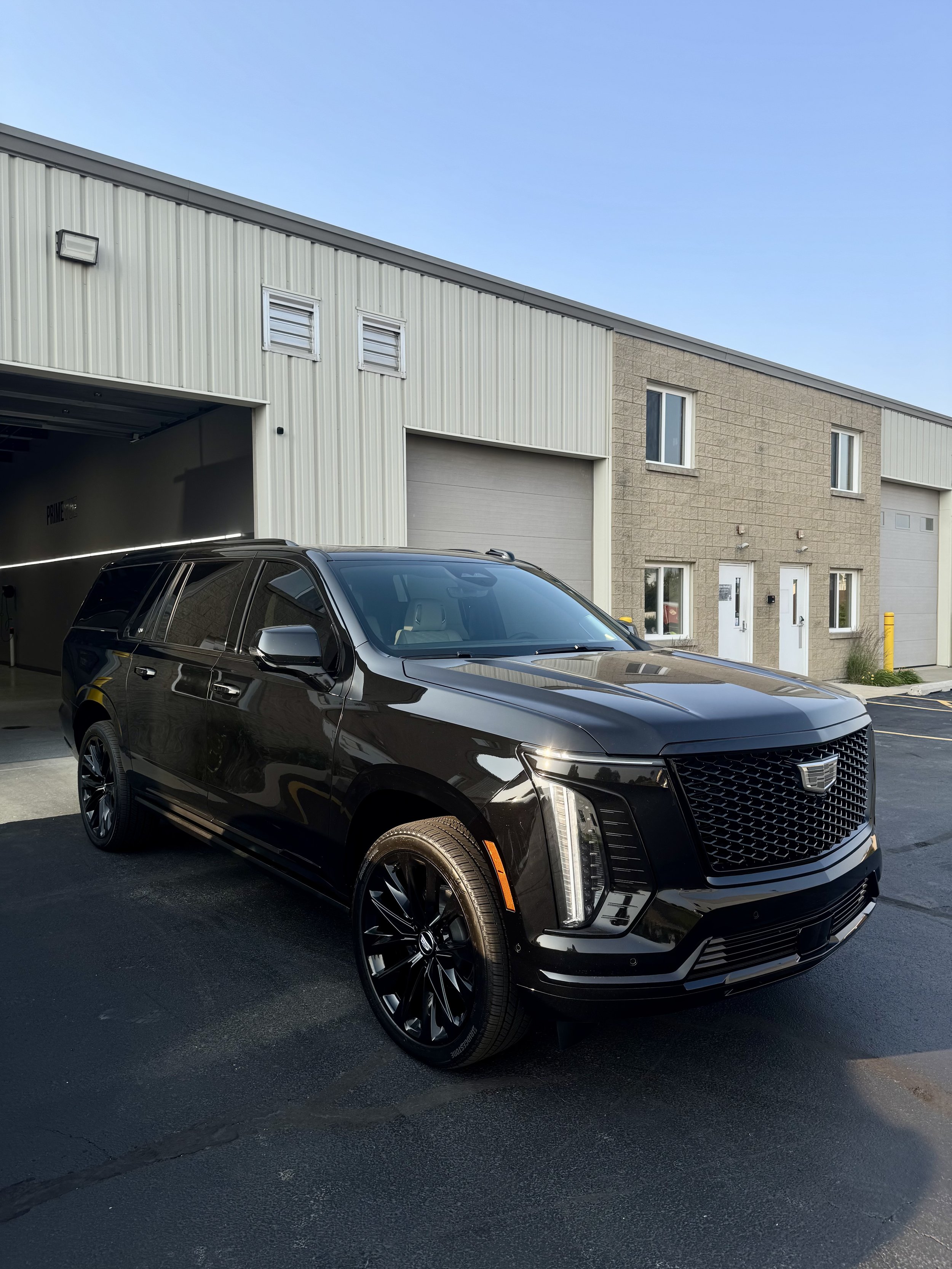 Black Cadillac SUV parked outside a modern building with metal siding and brick accents under a clear blue sky.