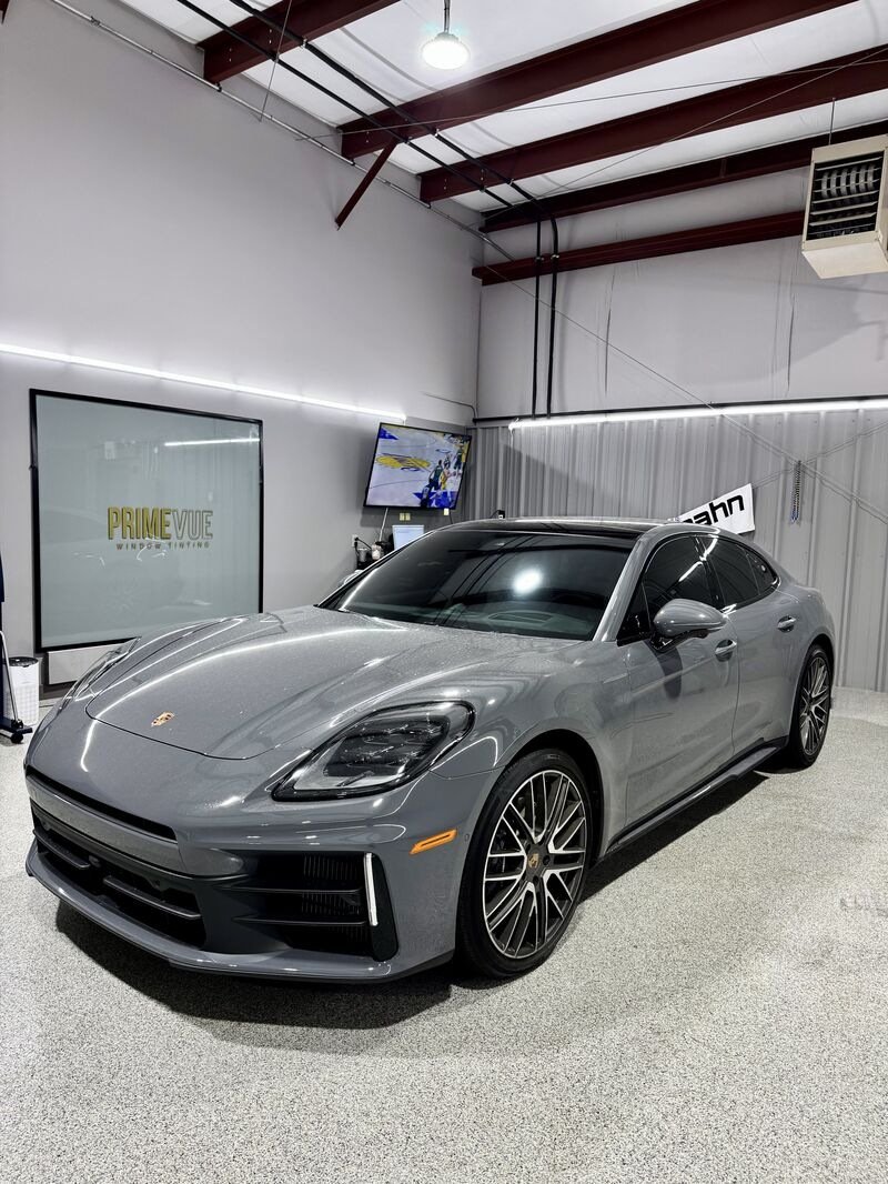Gray luxury sports car inside a showroom with industrial ceiling and wall-mounted monitors, one displaying 'PrimeView Window & Lighting'.