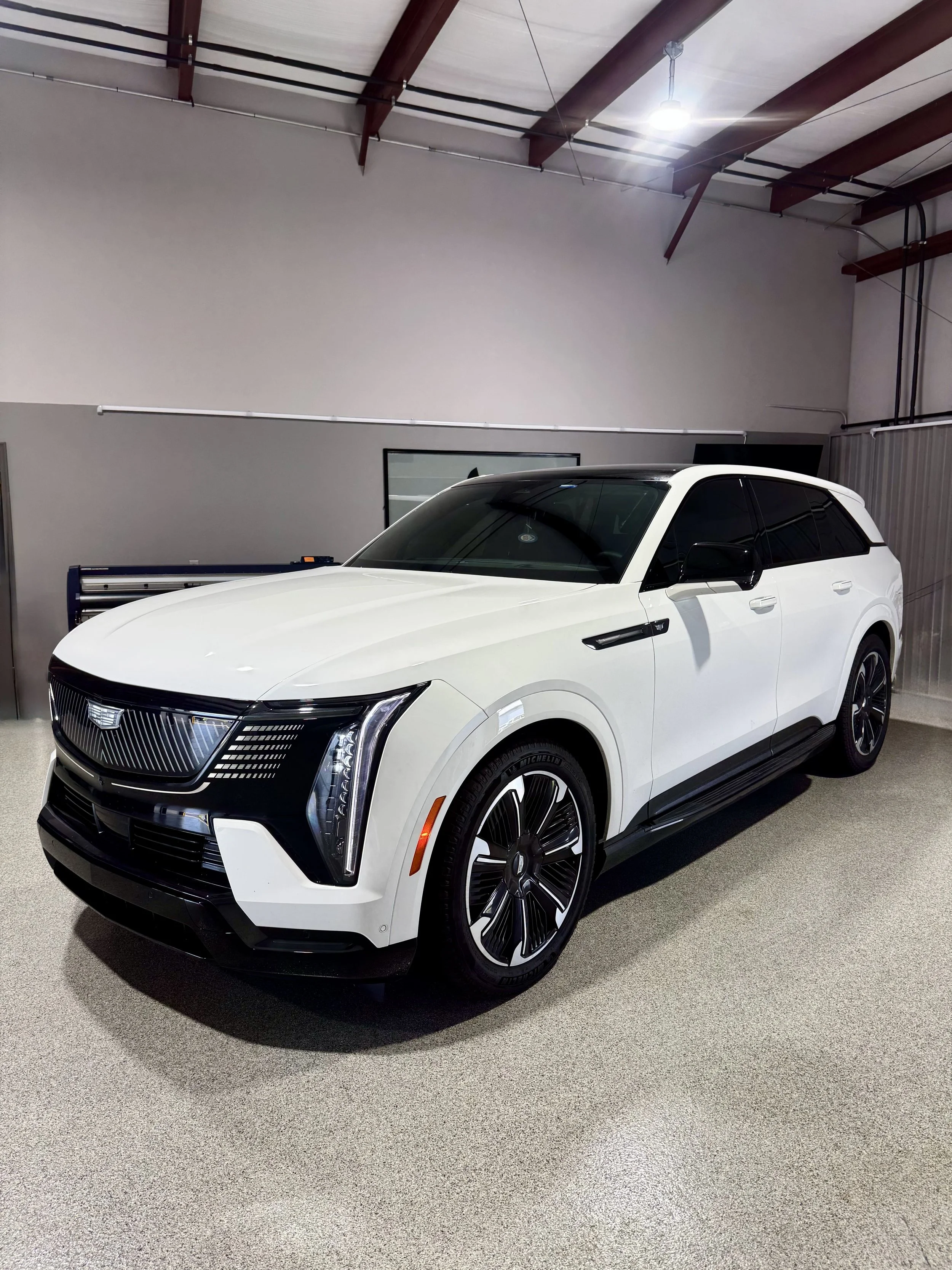 A white Cadillac SUV parked indoors on a textured grey floor, with a grey wall and a window in the background.