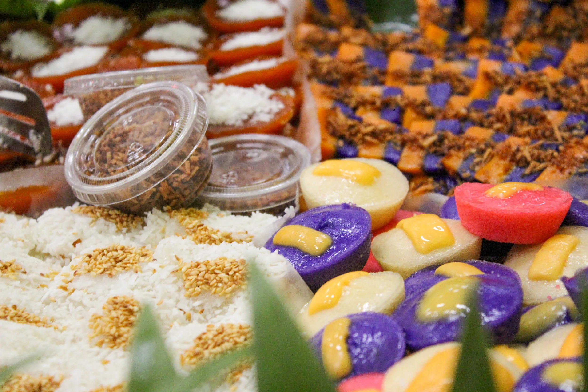 Colorful assortment of traditional Mexican sweets, including candied fruits, plum-colored and white candies topped with yellow glaze, and small containers of crushed nuts.