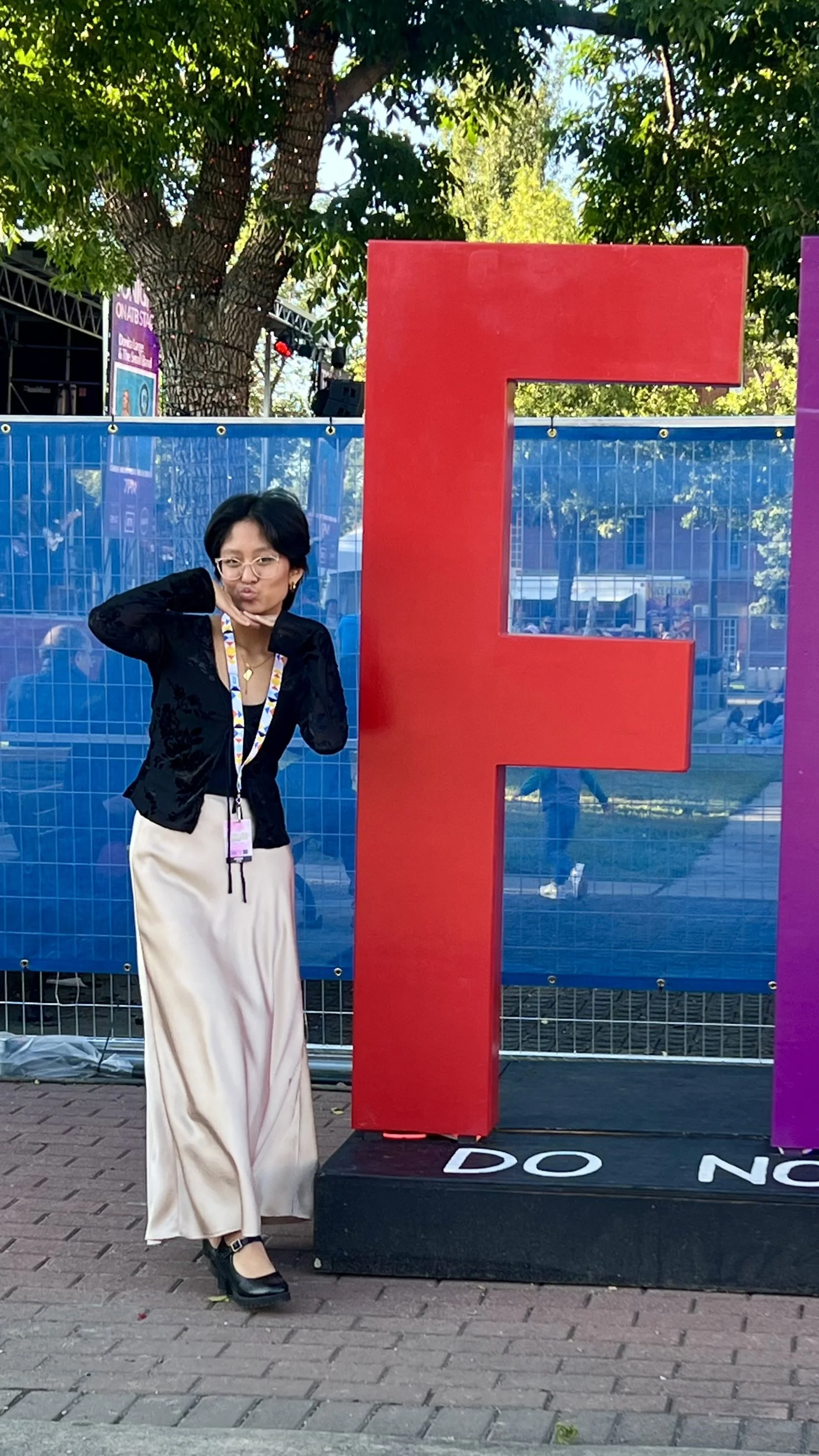 Woman standing next to a large red letter "E" at an outdoor event or festival.