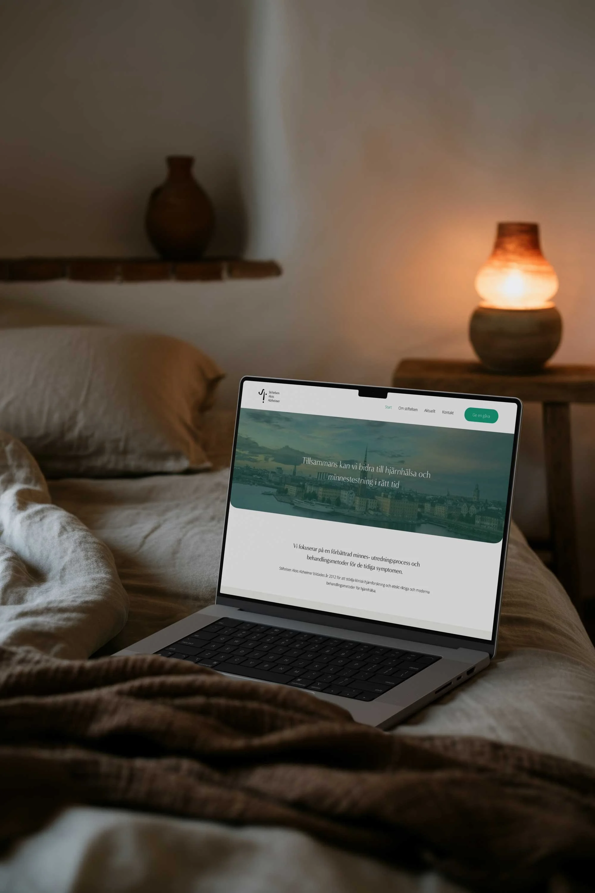 Mac med Stiftelsen Alzheimers hemsida på säng med mysig belysning. Therese Squarespace webbdesigner