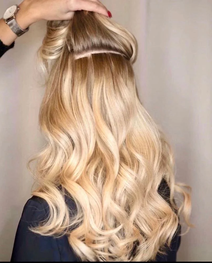 Back view of a woman with long, wavy blonde hair being styled.