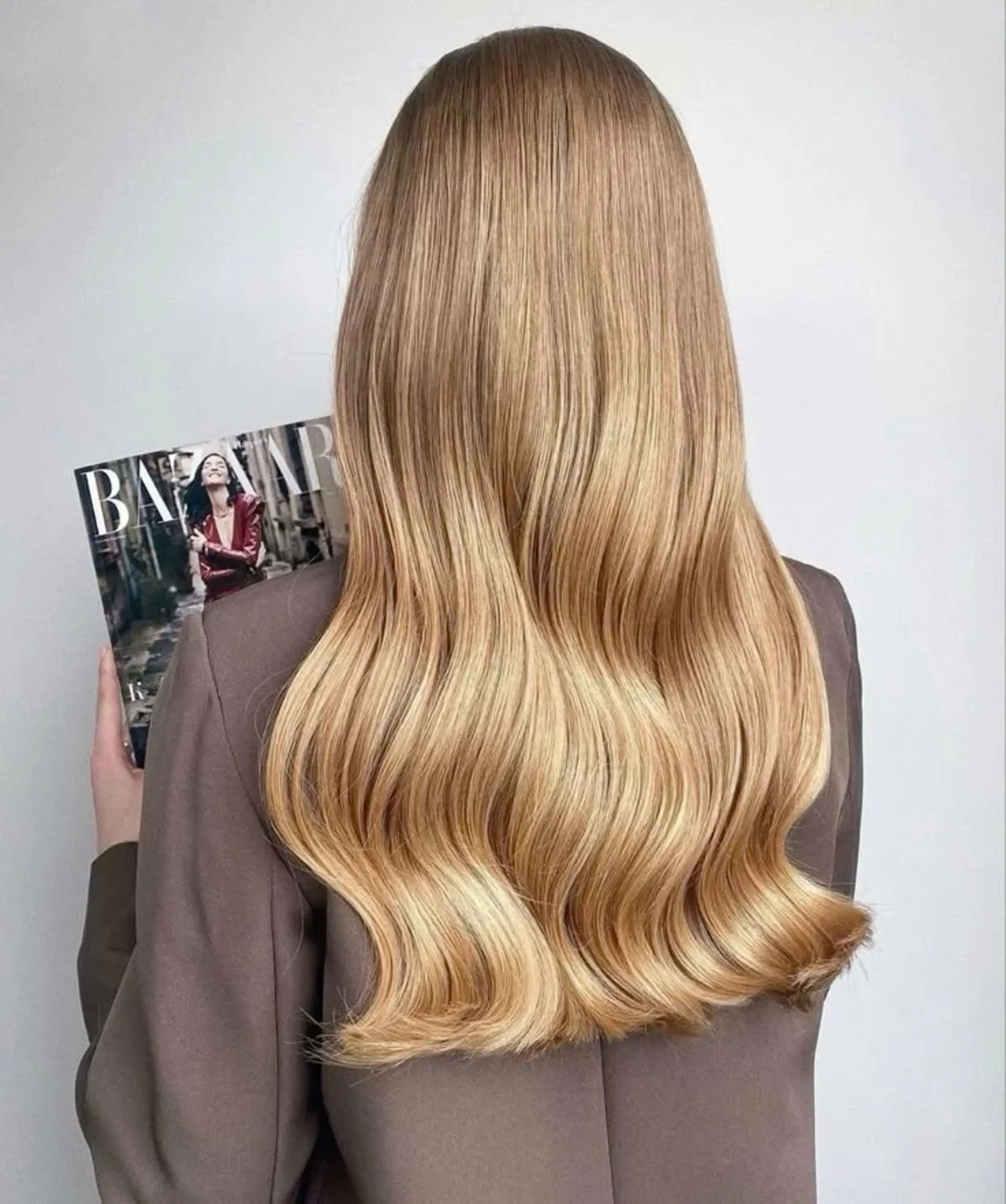 Back of woman with long, wavy blonde hair holding a magazine.