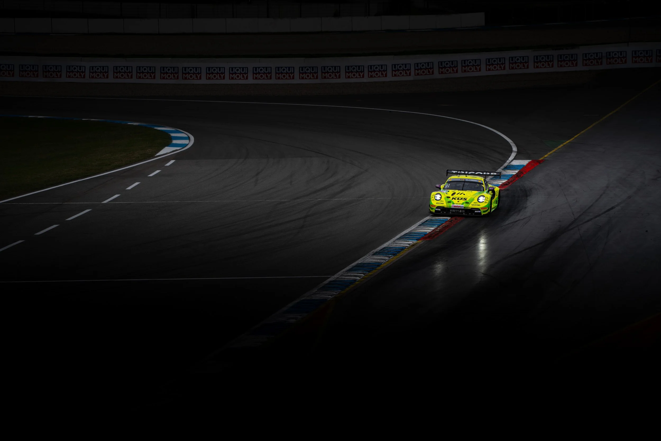 A bright yellow race car with sponsor logos on a dark racetrack, turning sharply as it navigates a curve during a race at night.