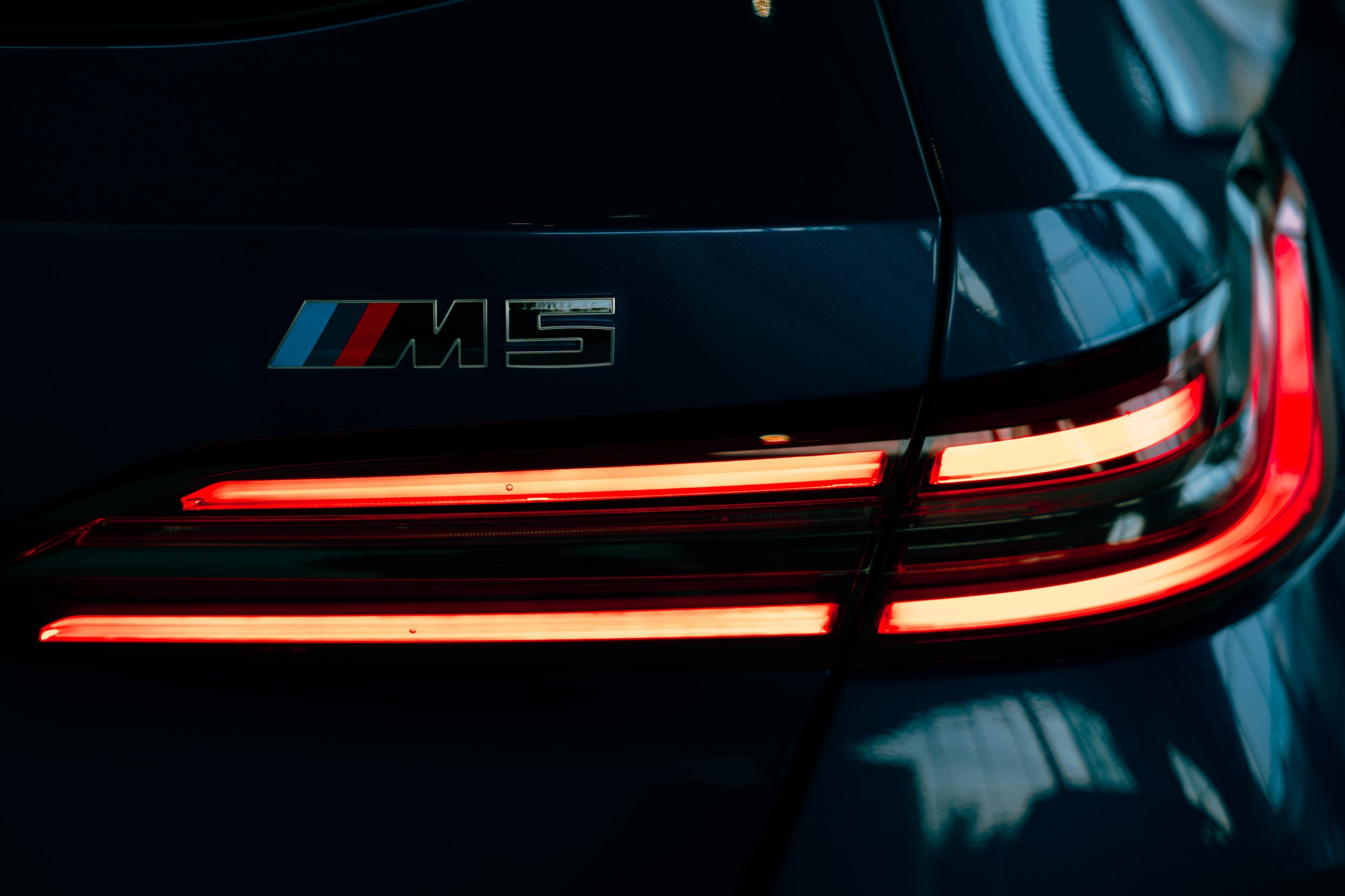 Close-up of the rear of a black BMW M5 car, showing illuminated taillights and the M5 badge.