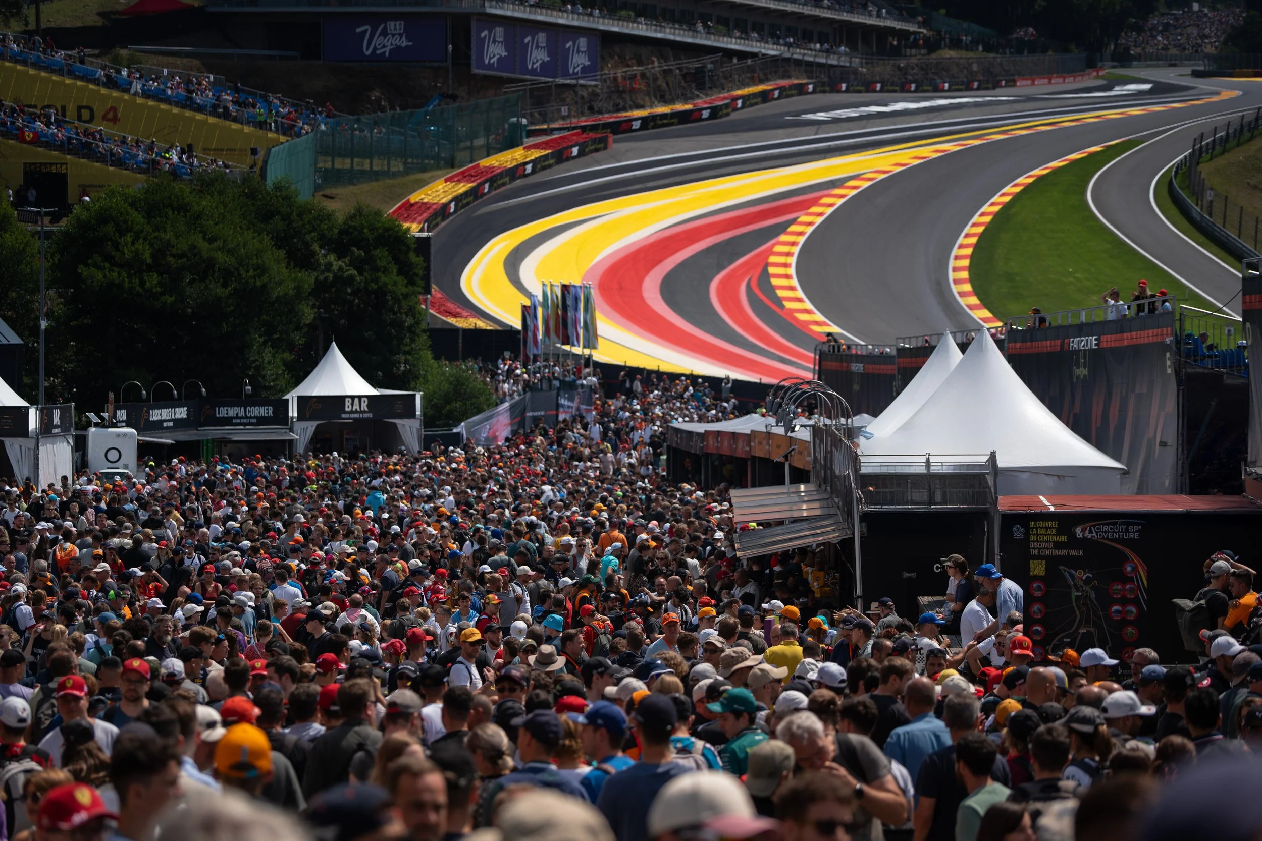 Crowd of people at a Formula 1 race in Las Vegas, with a view of the track, grandstands, and colorful barriers.